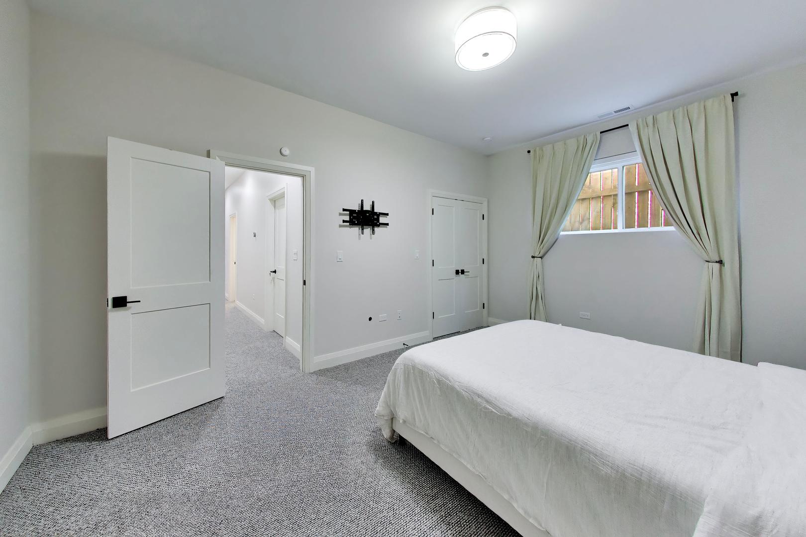 Bedroom with a white bed, patterned gray carpet, tied-back curtains, and a wall-mounted TV bracket.