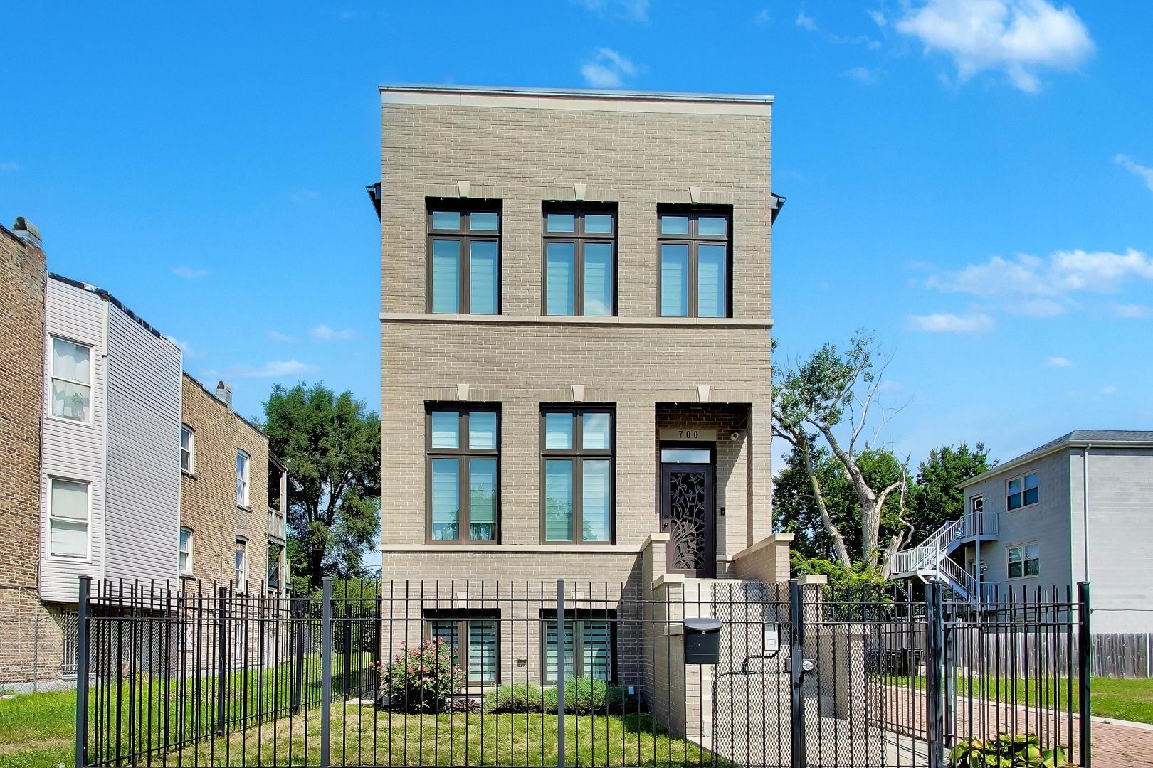 Three-story tan brick house with tall windows, a recessed entrance, and a black metal front fence.