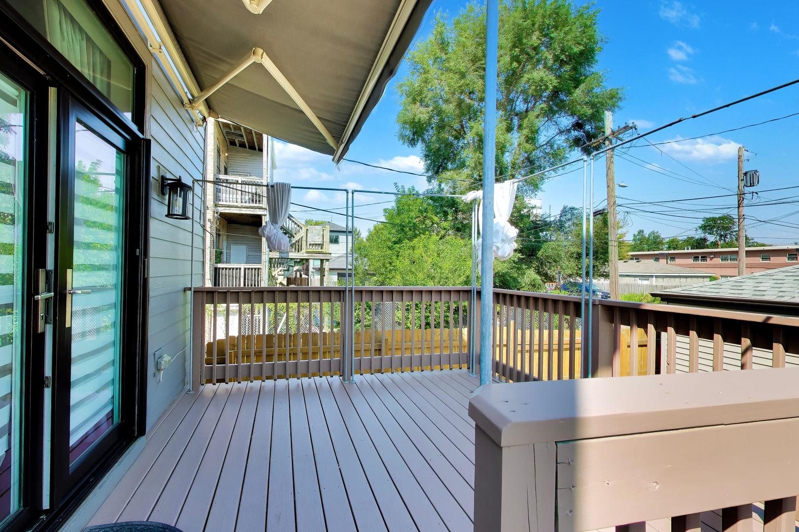 Raised deck with a retractable awning, gray flooring, and views of neighboring homes and trees.