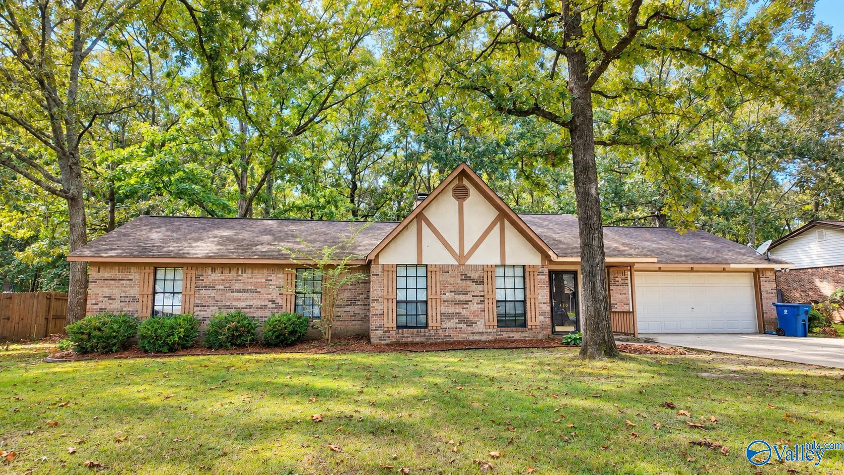 Brick ranch house with a timber-trimmed gable and attached garage beneath a large leafy tree.