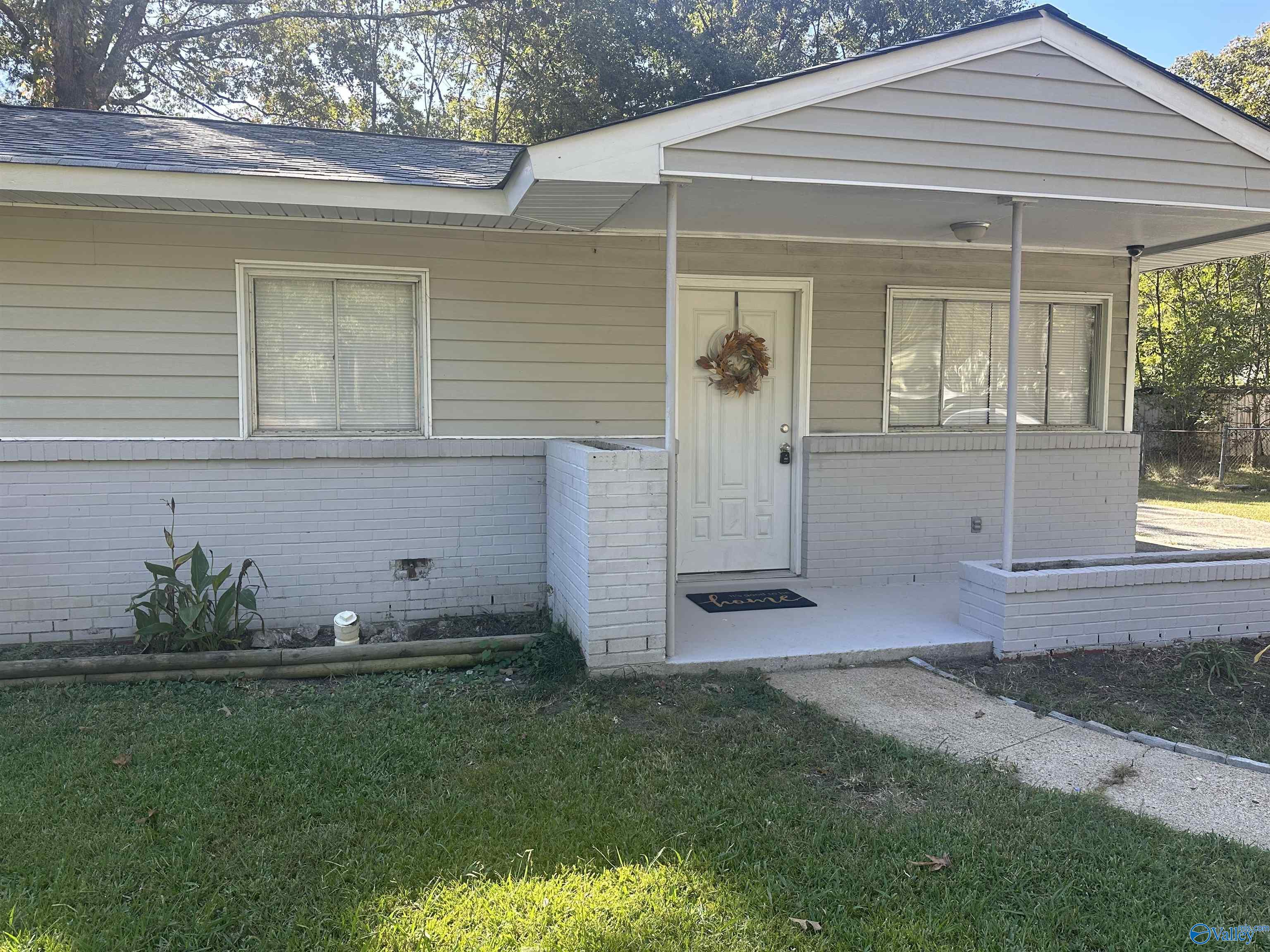 Single-story gray-sided house with a covered porch, white brick facade, and wreath on the front door.