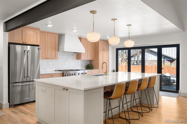 Modern kitchen with a large white island, light wood cabinets, and sliding glass doors.