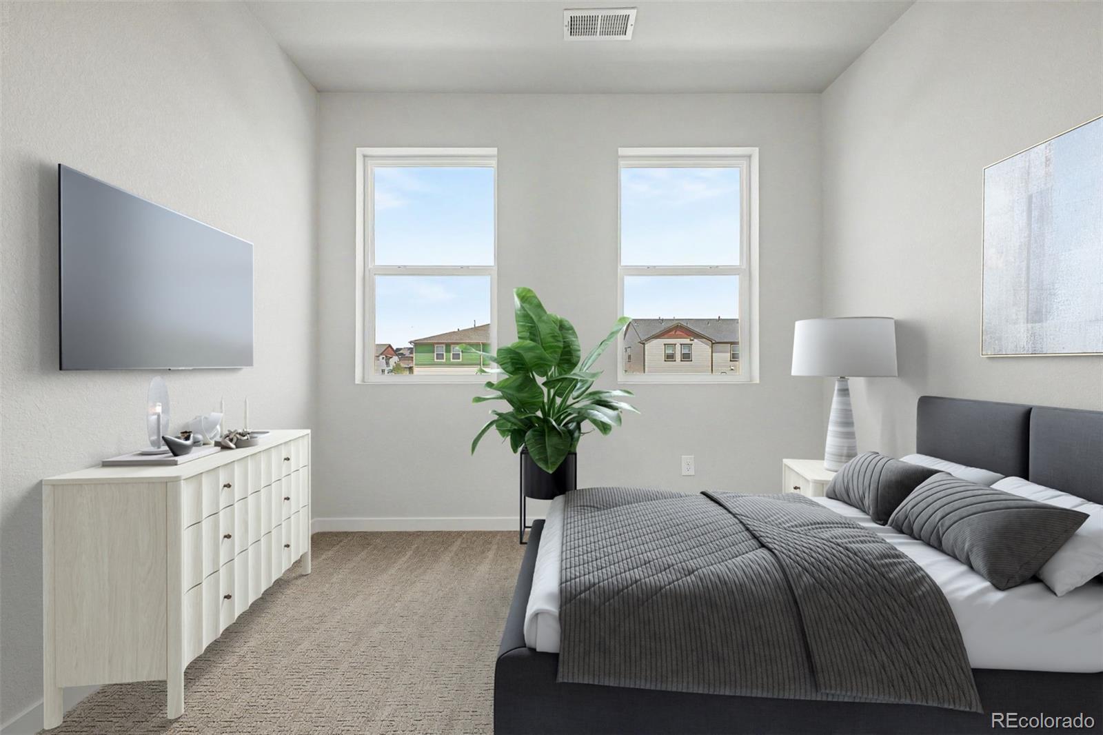 Furnished bedroom with a gray bed, white dresser, wall-mounted TV, and two windows.