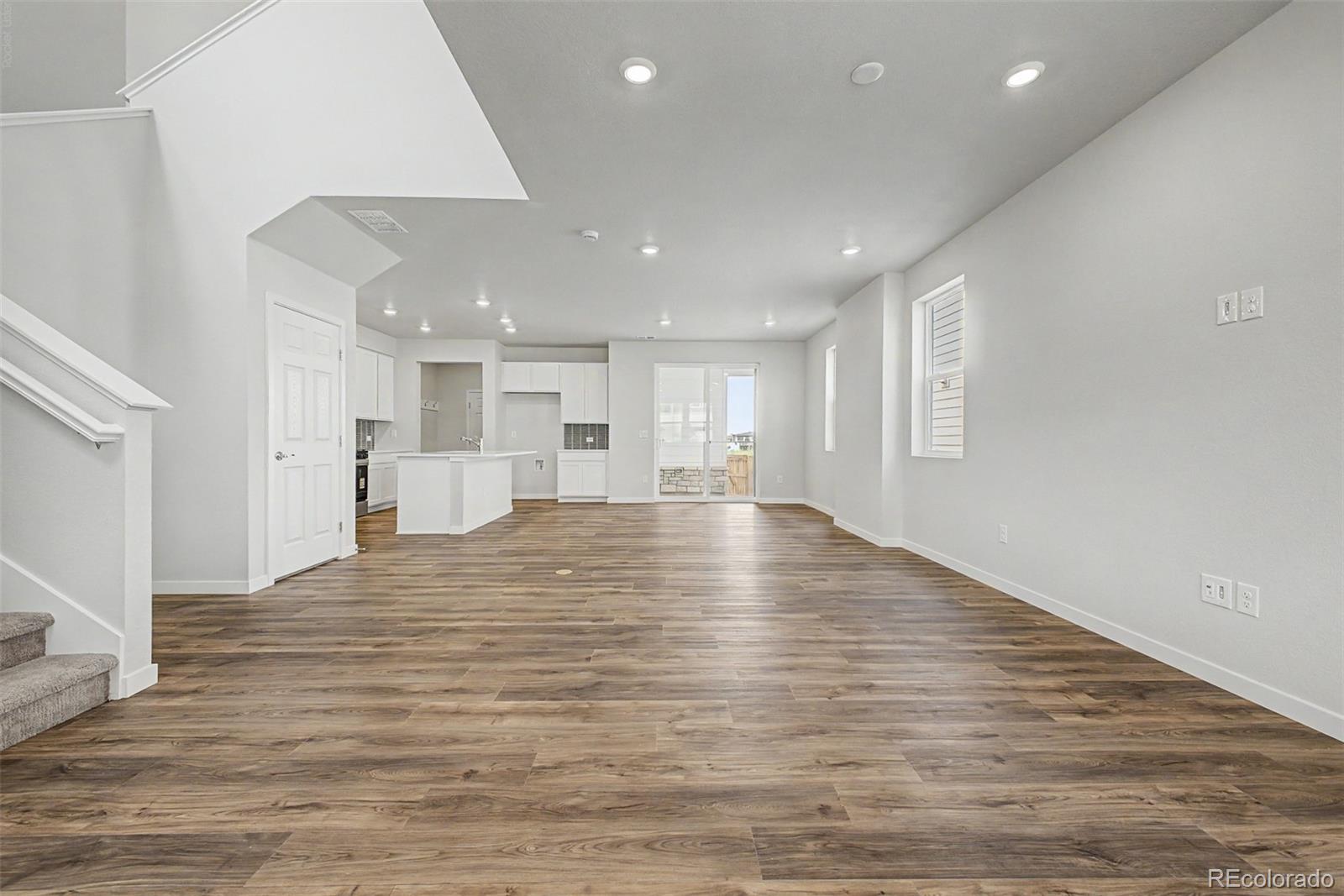 Open-plan living area with wood-look flooring, staircase, kitchen island, and sliding glass doors.