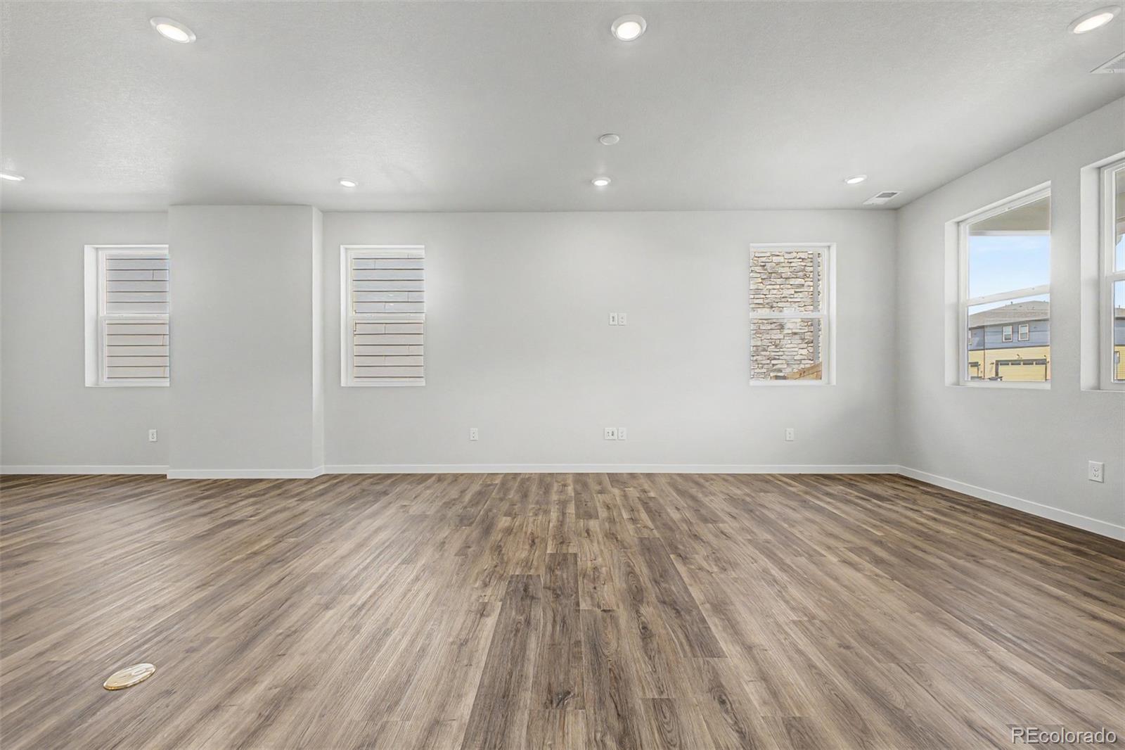 Vacant room with wood-look flooring, gray walls, and multiple windows.