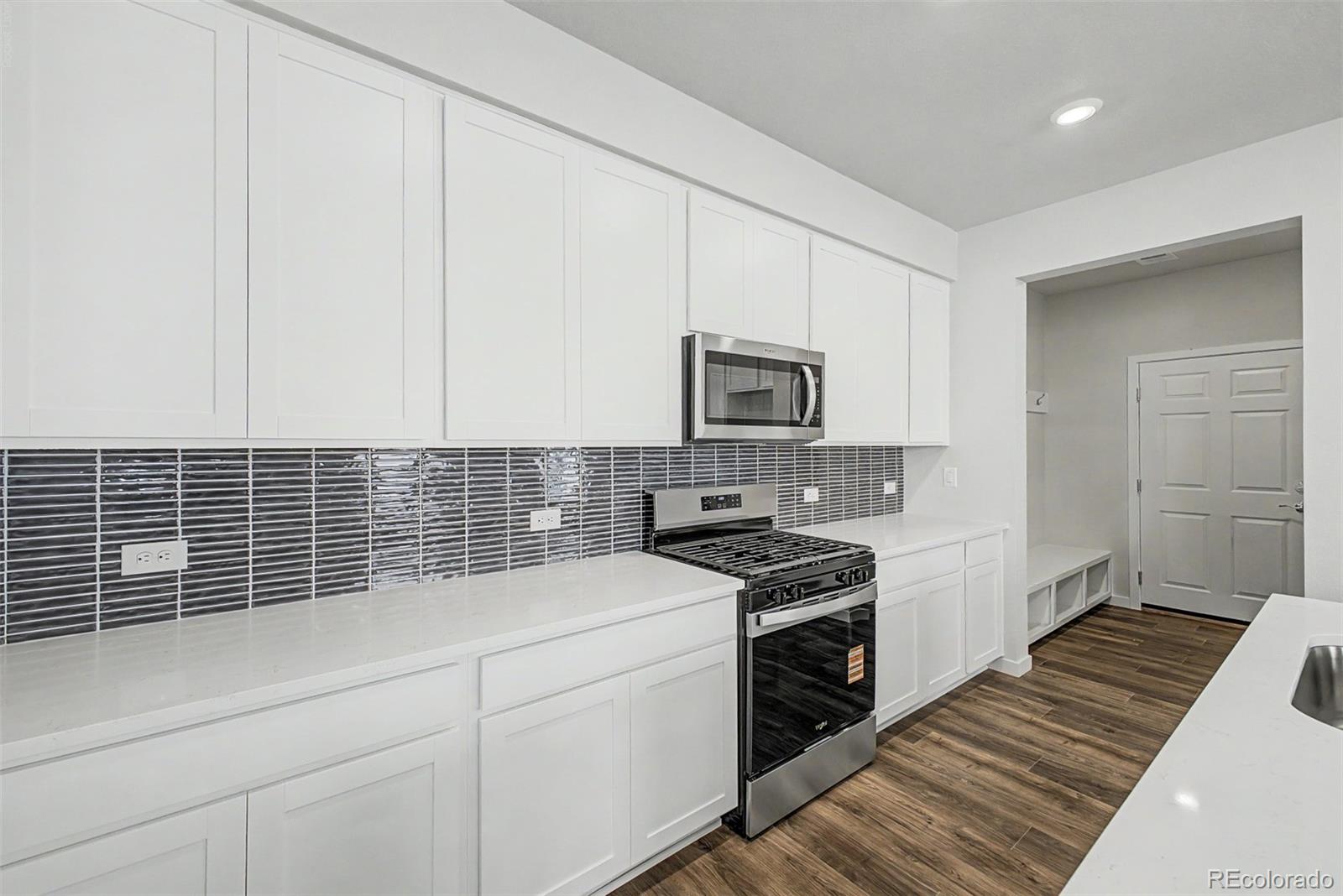 Kitchen with white cabinetry, dark tile backsplash, and a stainless steel gas range.