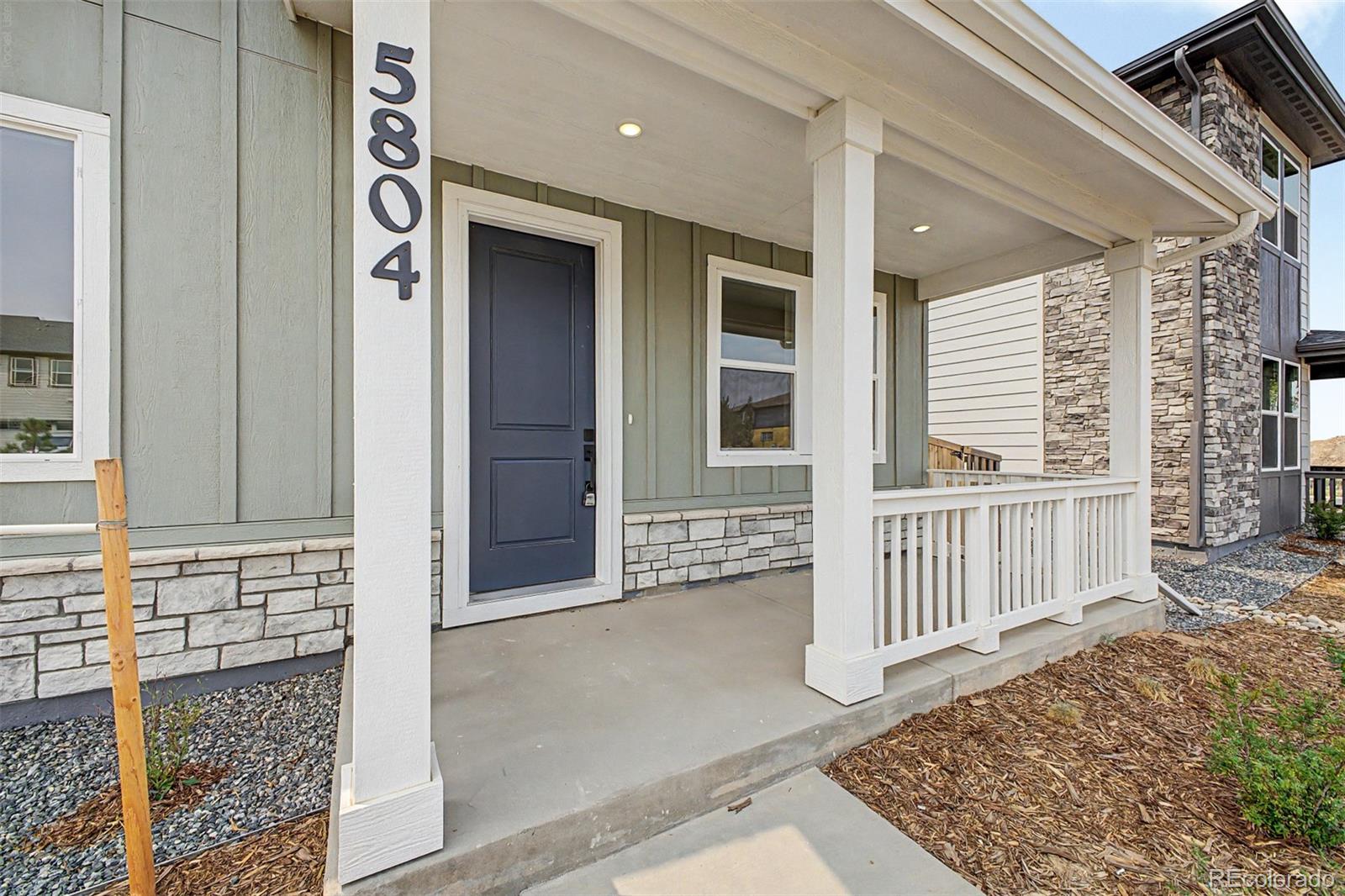 Covered front porch with a dark blue door, white railings, and stone veneer.