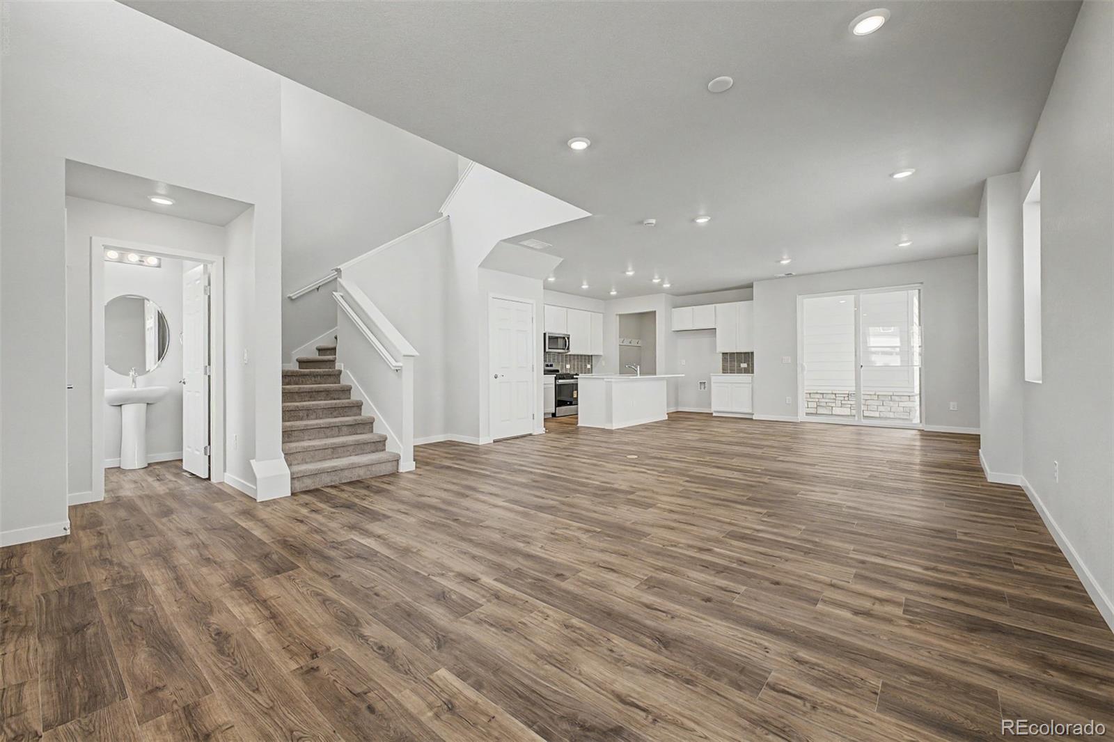 Open living room with wood-look floors, carpeted stairs, and a white kitchen.