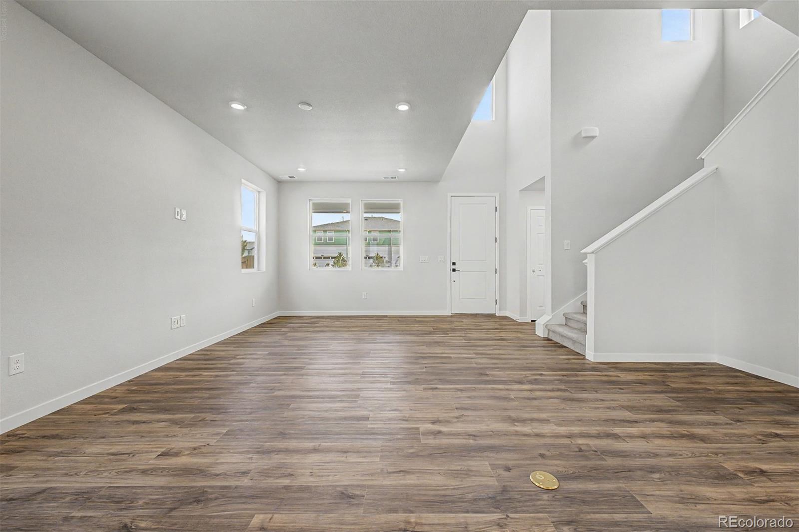 Empty living room with wood-look floors, tall ceiling, and a carpeted staircase.