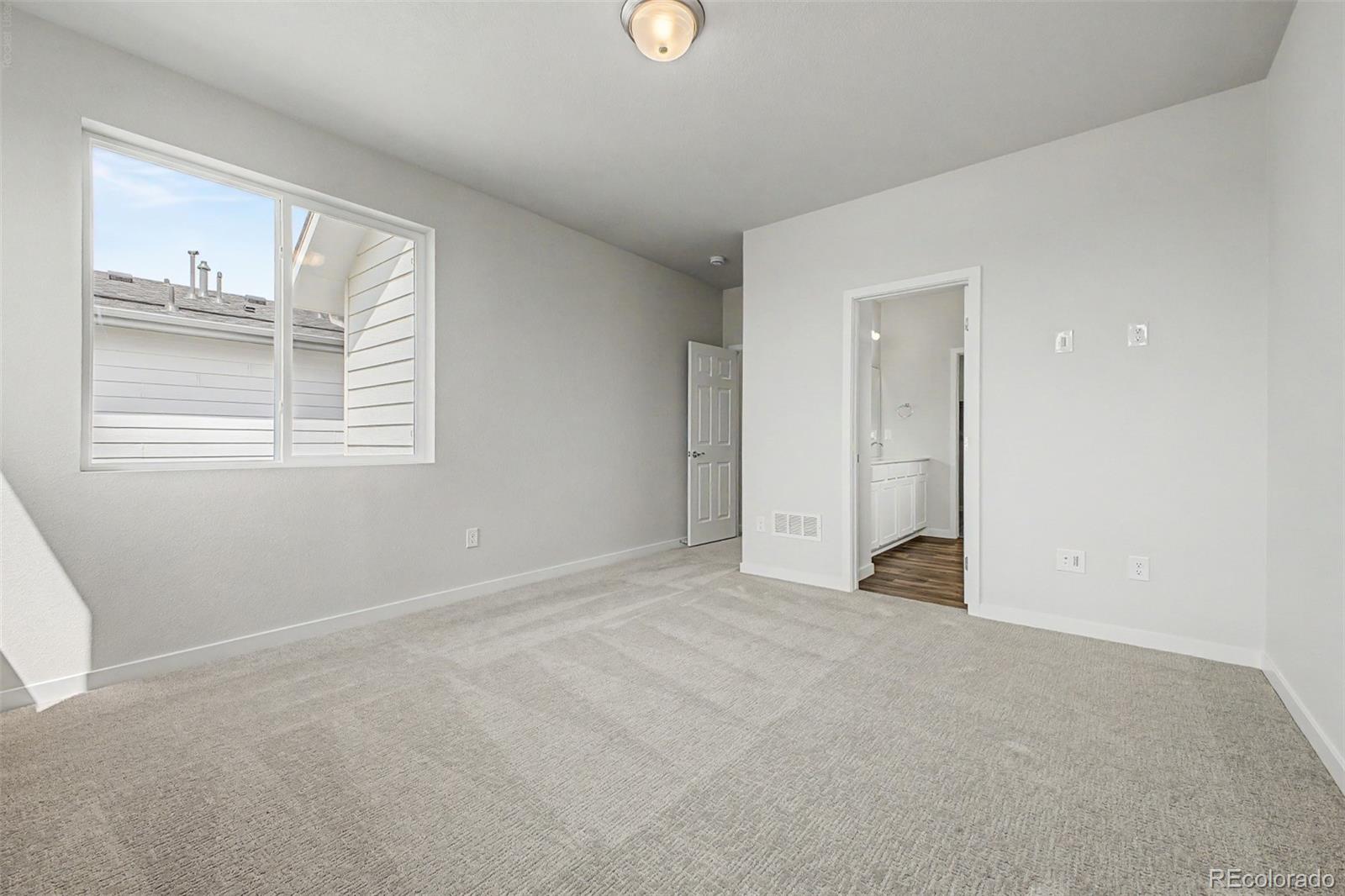 Empty carpeted bedroom with a large window and doorway to an adjoining bathroom.