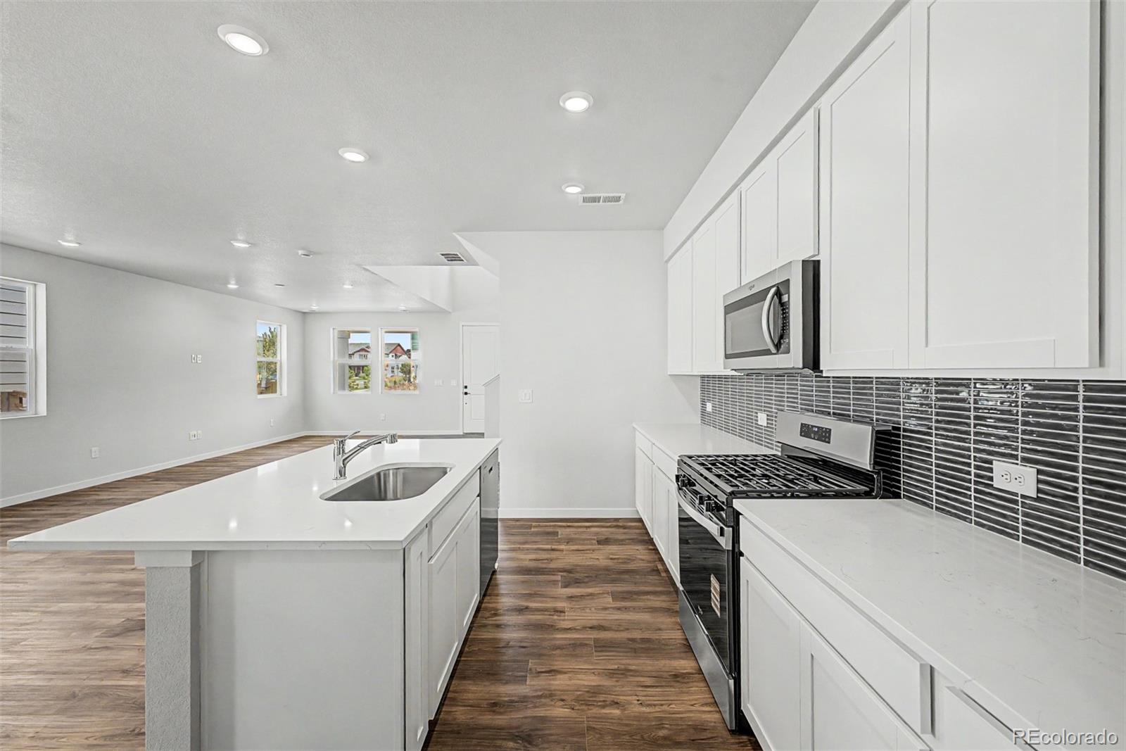 Open kitchen with white cabinets, a large island, dark tile backsplash, and wood-look floors.
