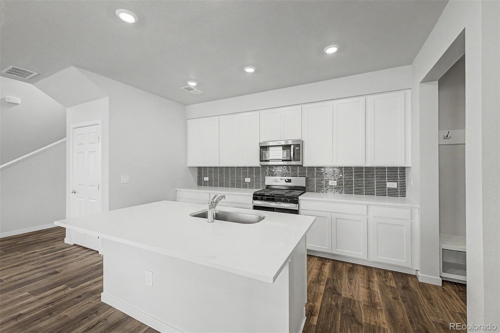 Kitchen with a large white island, white cabinets, stainless steel appliances, and wood-look floors.