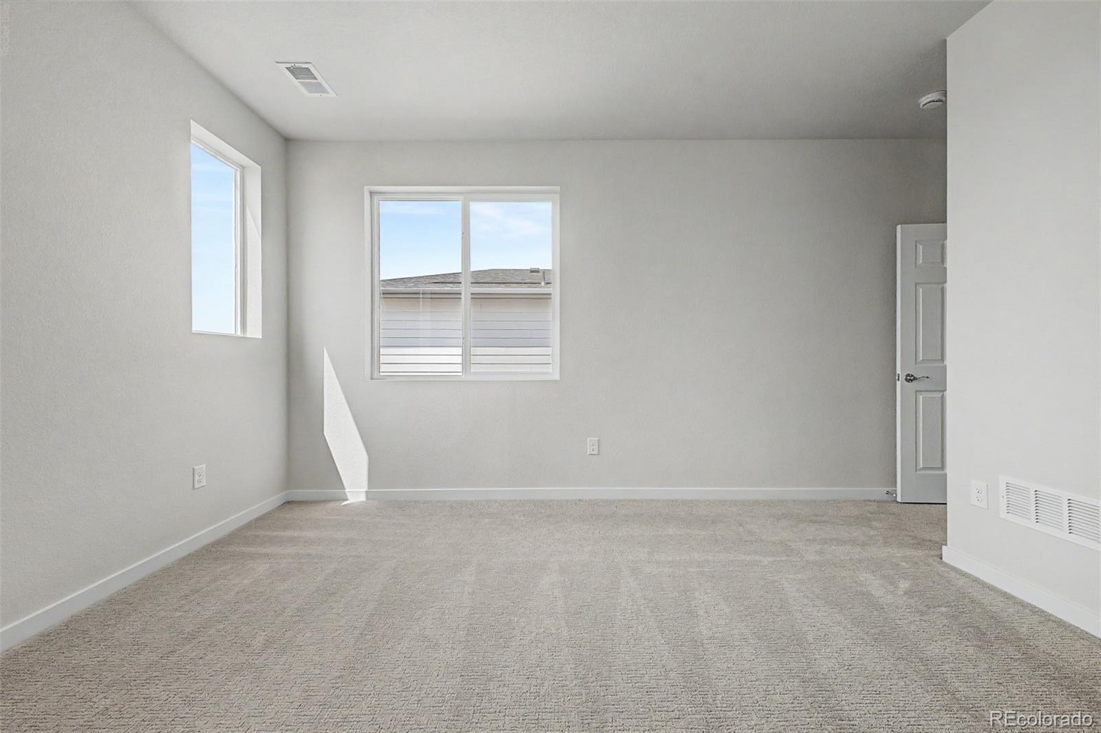 Empty carpeted bedroom with two windows and an open door.