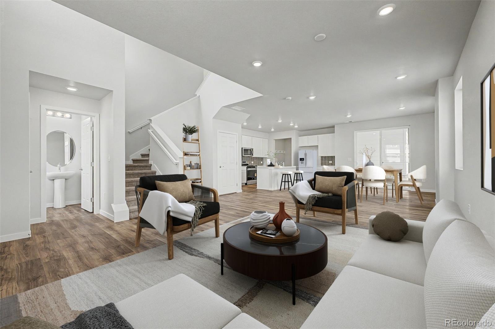 Staged open-plan living room with a round coffee table, staircase, and kitchen dining area.