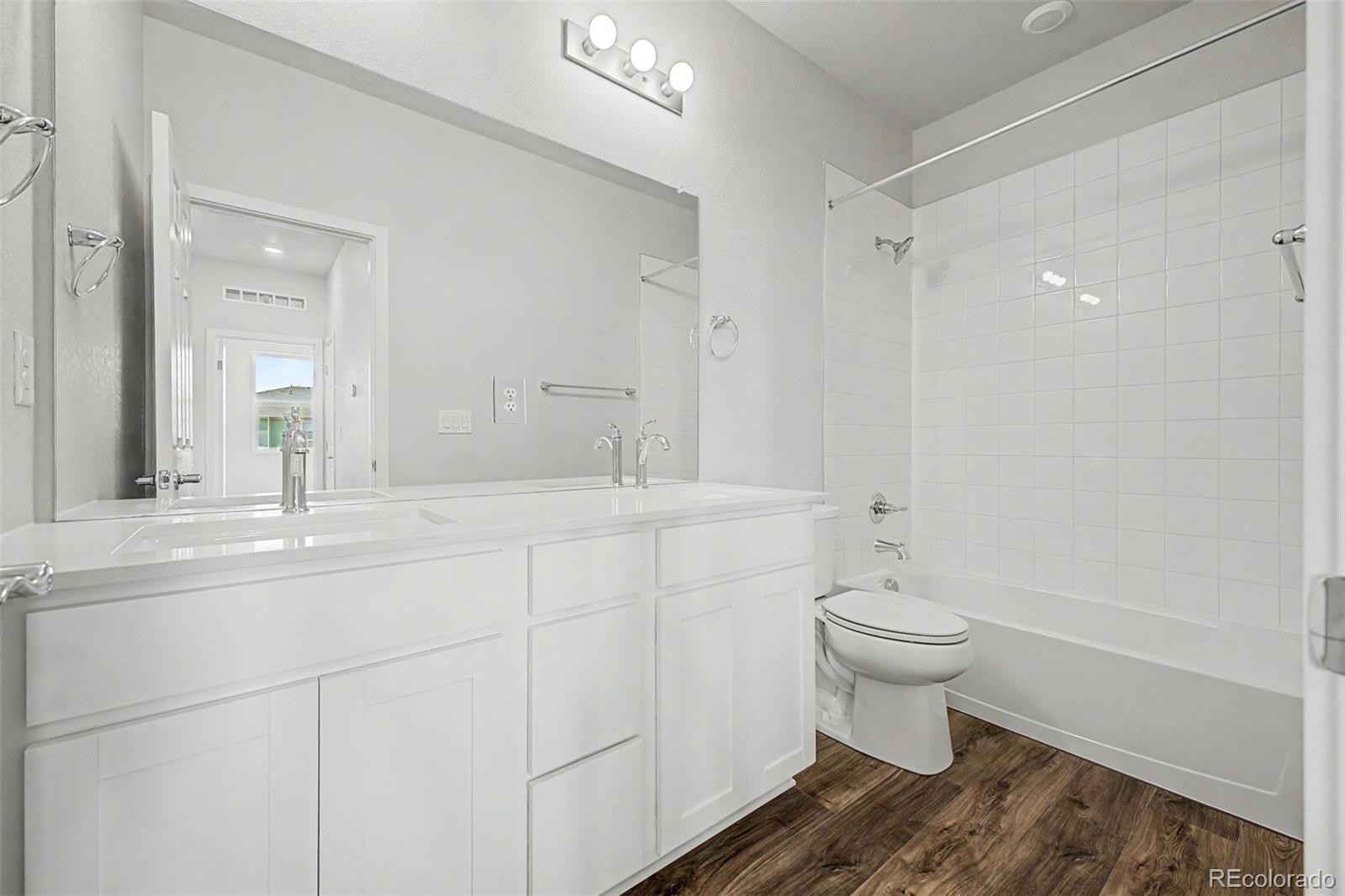 Bathroom with a long double-sink vanity, large mirror, and white-tiled tub and shower.