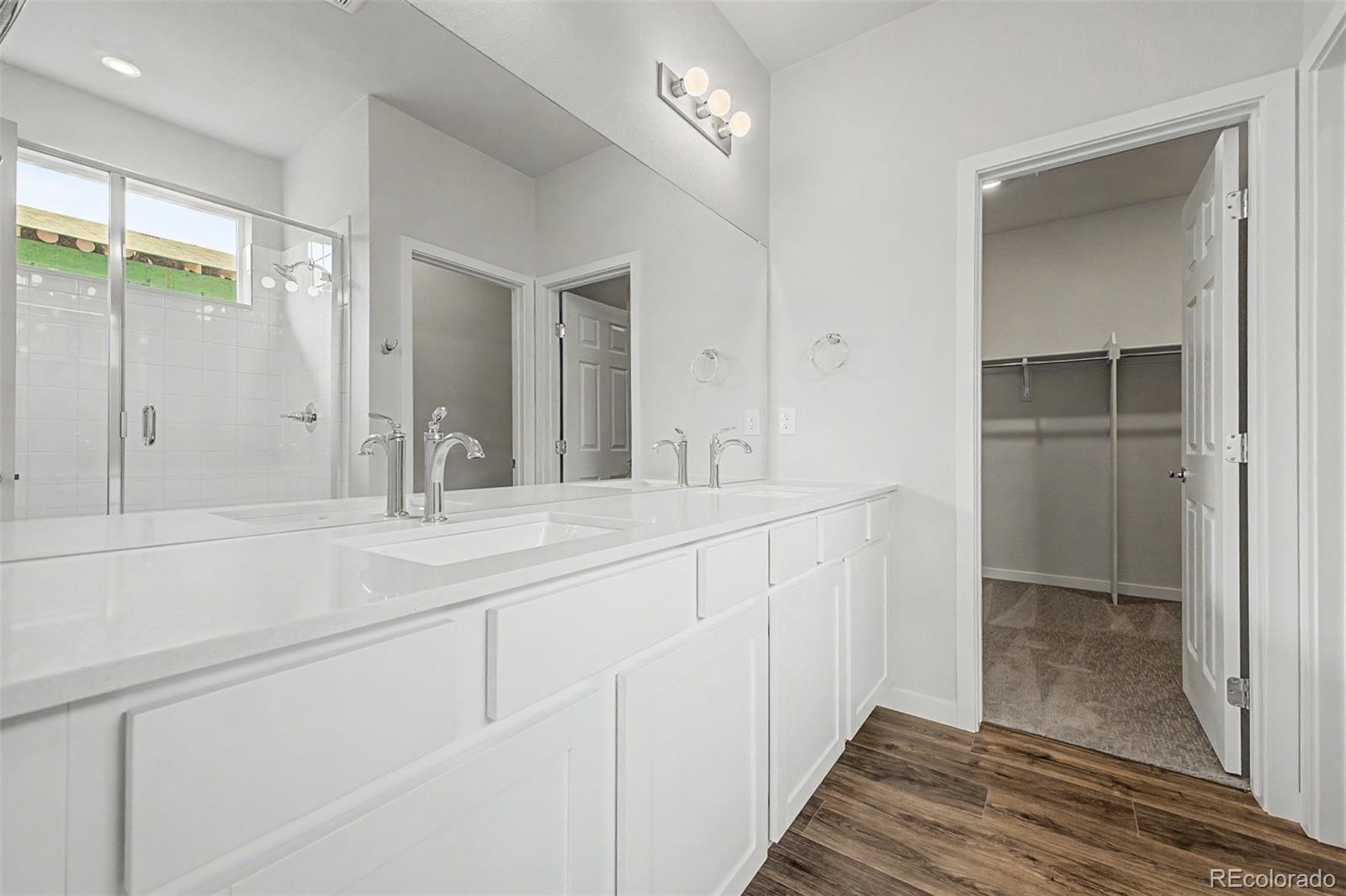 Primary bathroom with a double-sink vanity, glass shower, and doorway to a walk-in closet.