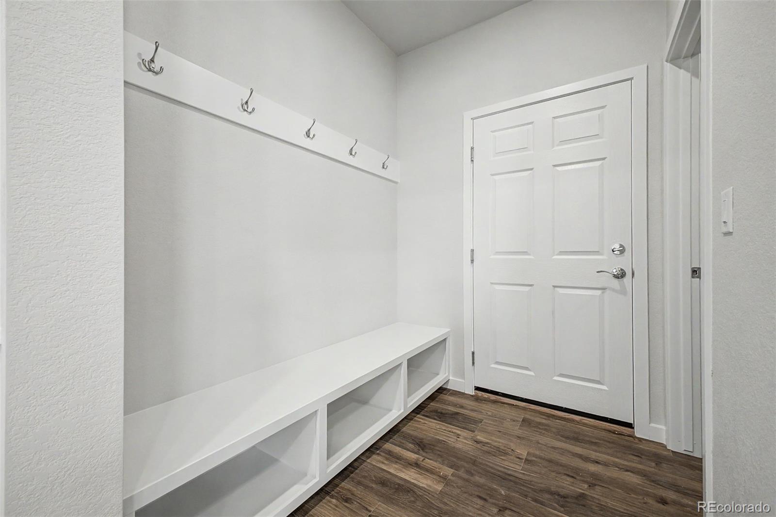 Entryway with a built-in bench, open cubbies, wall hooks, and dark wood-look flooring.