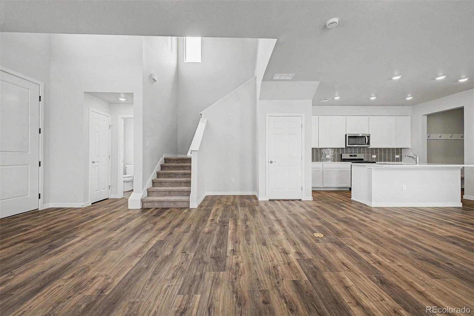 Open living area with wood-look floors, staircase, and white kitchen with island.