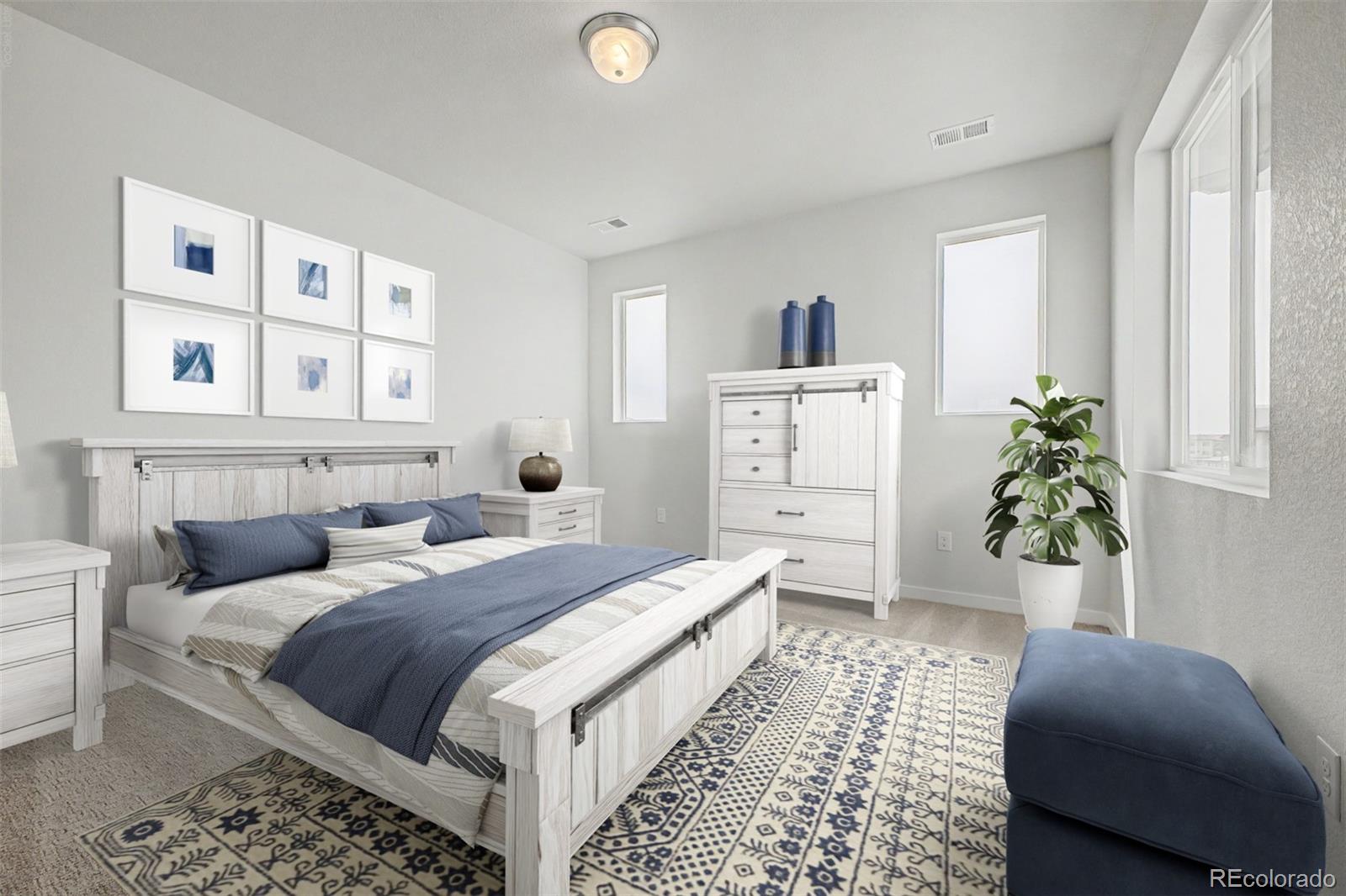Staged bedroom with a whitewashed wood bed, blue bedding, patterned rug, and large windows.
