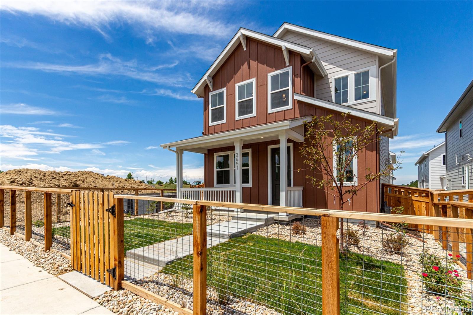 Two-story red-brown house with a covered porch and fenced front yard.