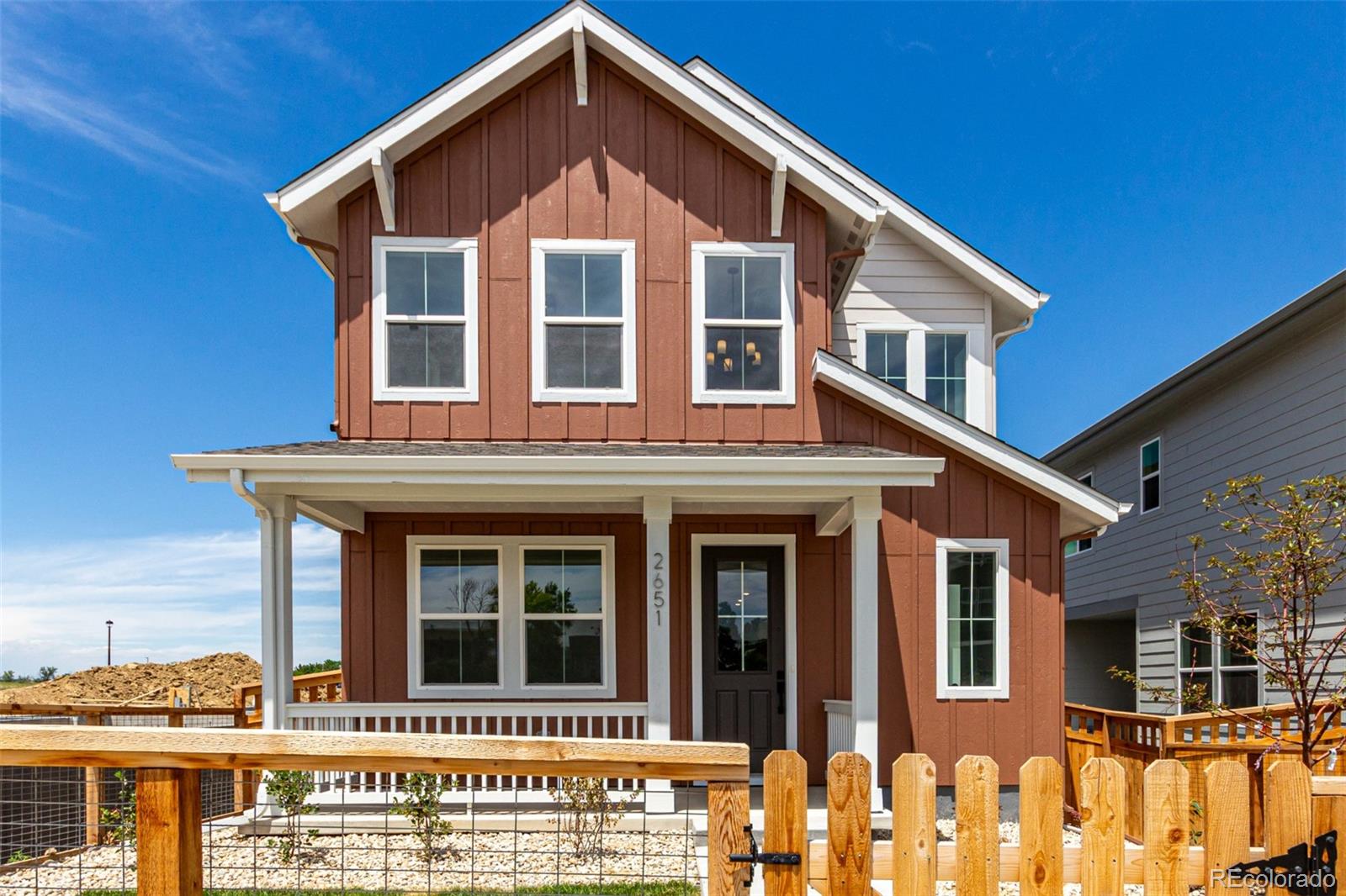Two-story reddish-brown house with white trim, a covered porch, and wooden fence.