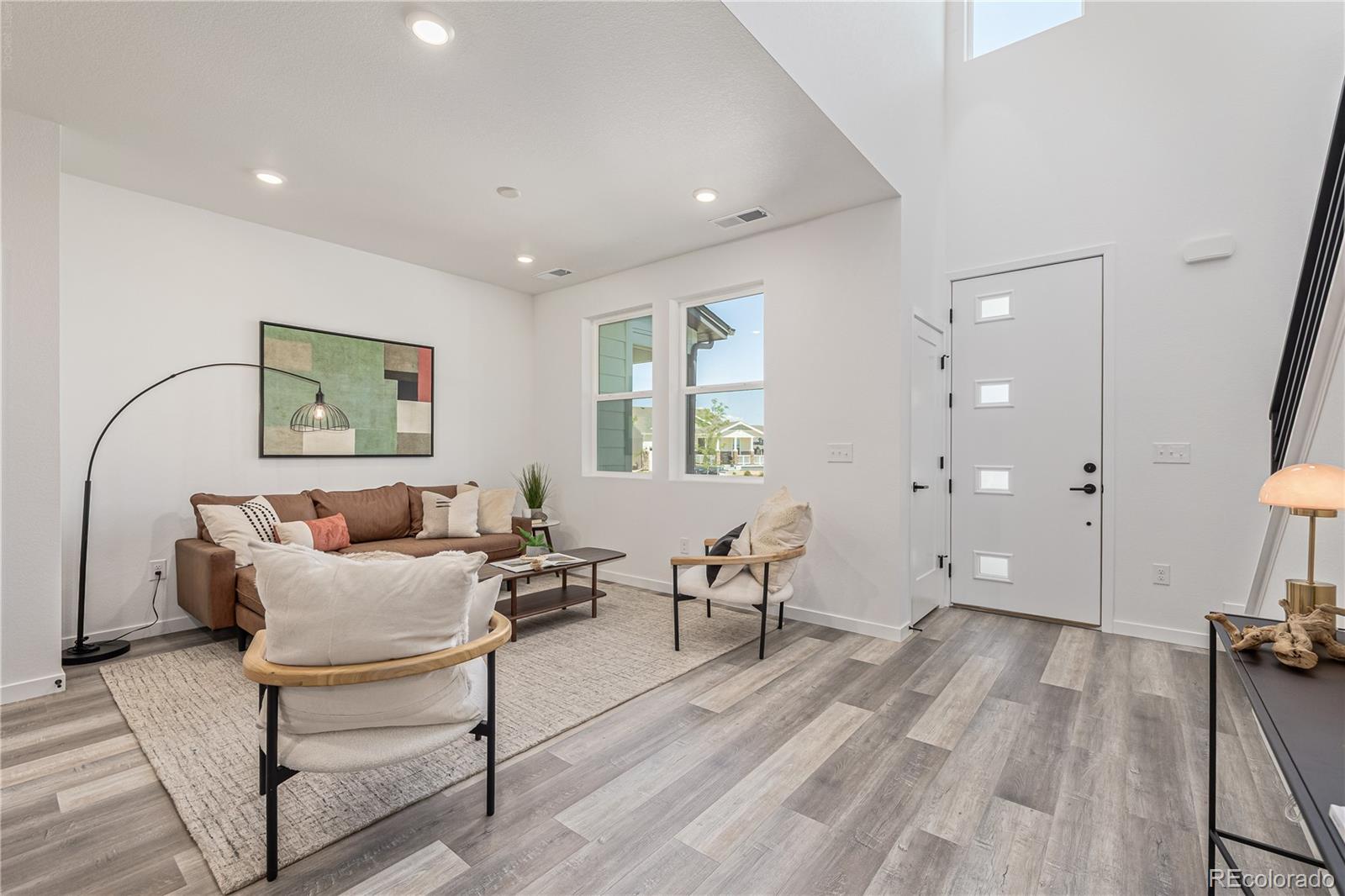 Staged living room with a brown sofa, light accent chairs, and gray wood-look flooring.