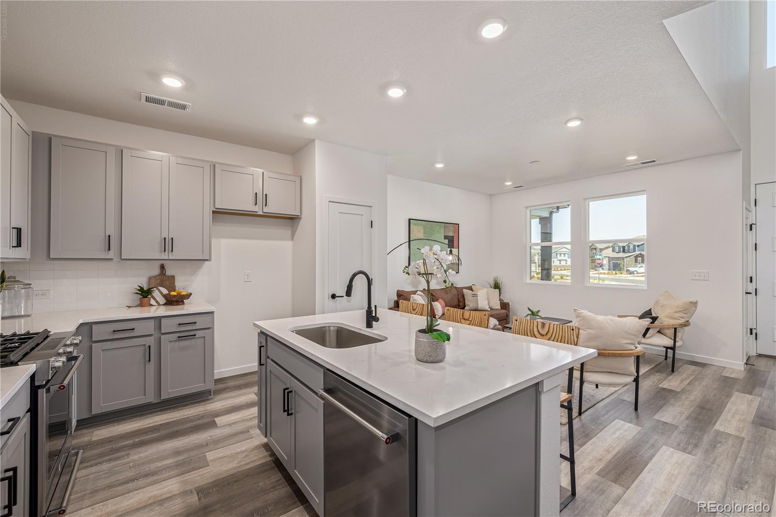 Open kitchen with a large white island, gray cabinets, and a furnished living area.