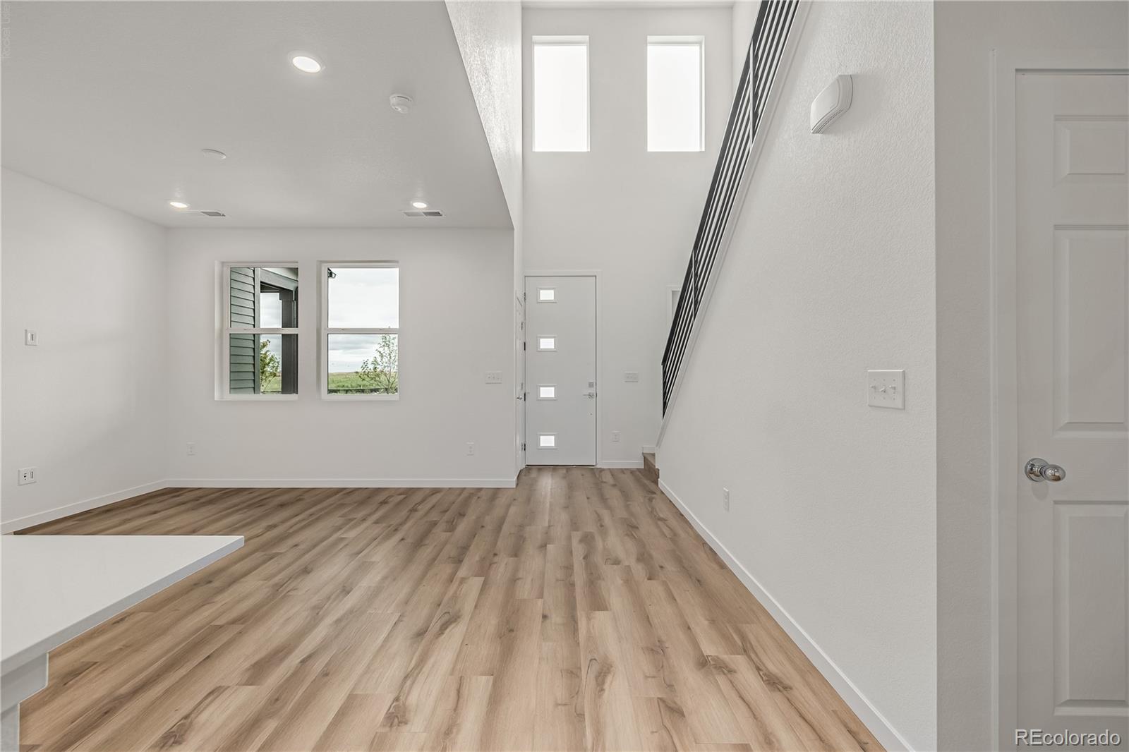 Vacant living area with wood-look floors, tall windows, and a staircase with black railing.