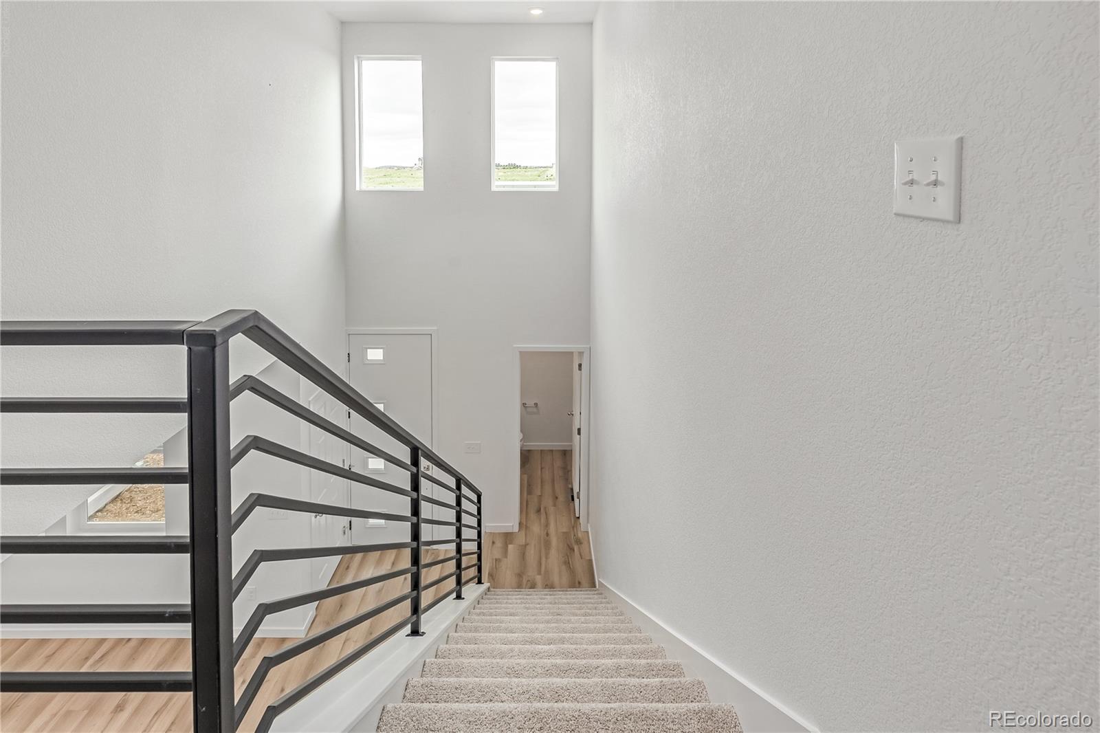 Carpeted staircase with black metal railing leading to a bright landing with tall windows.