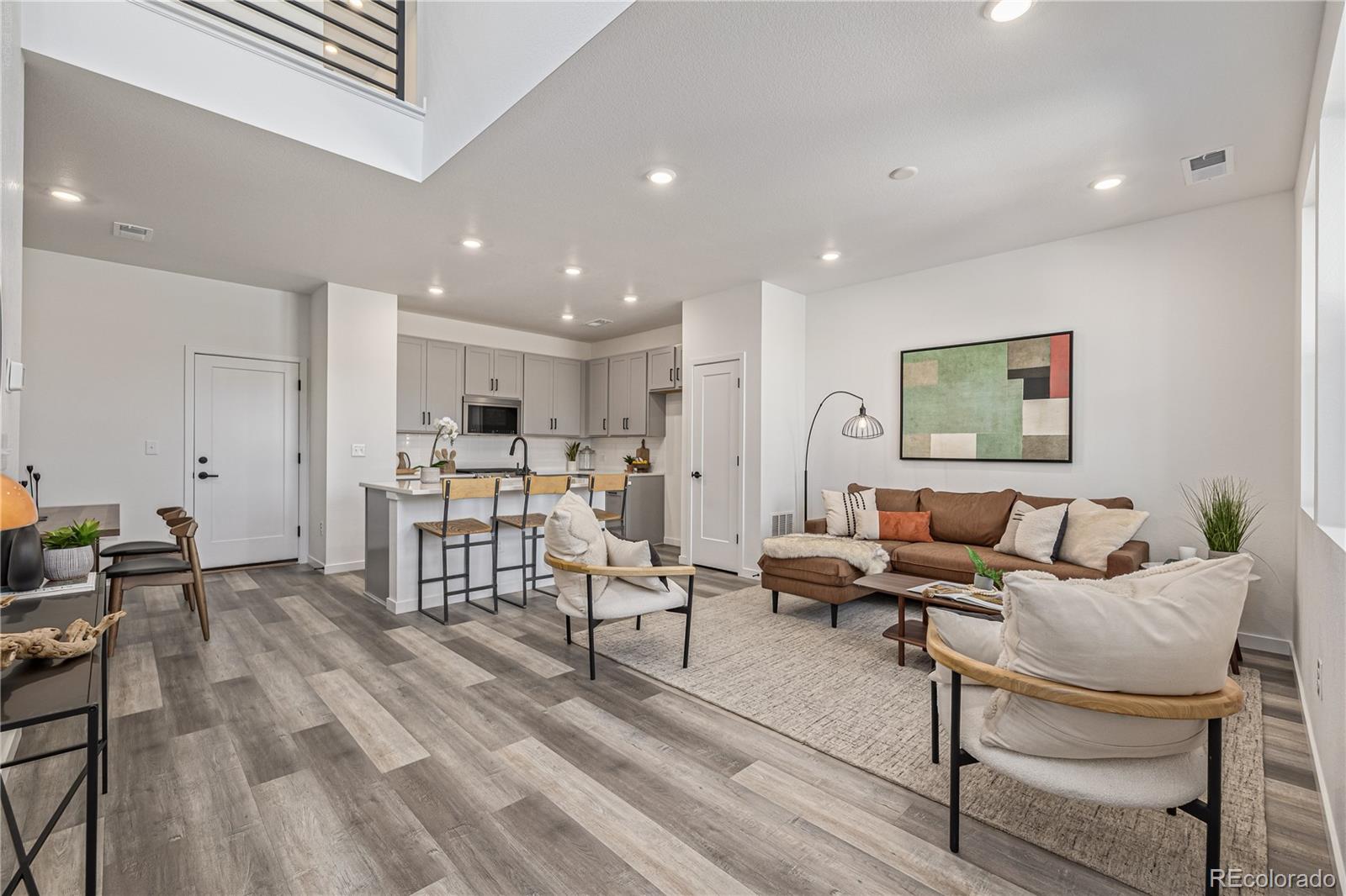 Open-plan living room and kitchen with a brown sectional, gray cabinetry, and a high ceiling.