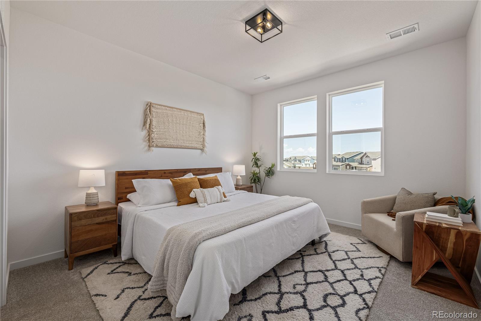 Staged bedroom with a king-size bed, white bedding, and two windows overlooking neighboring homes.