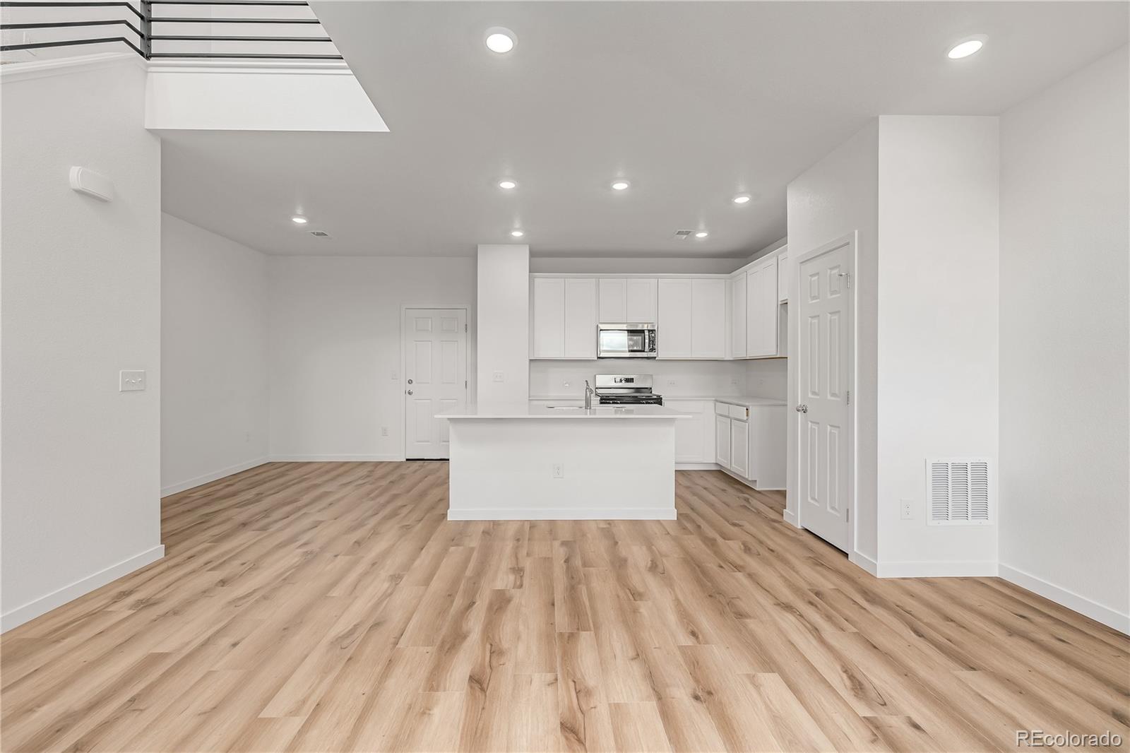 Unfurnished open living area and kitchen with a white island and light wood-look floors.