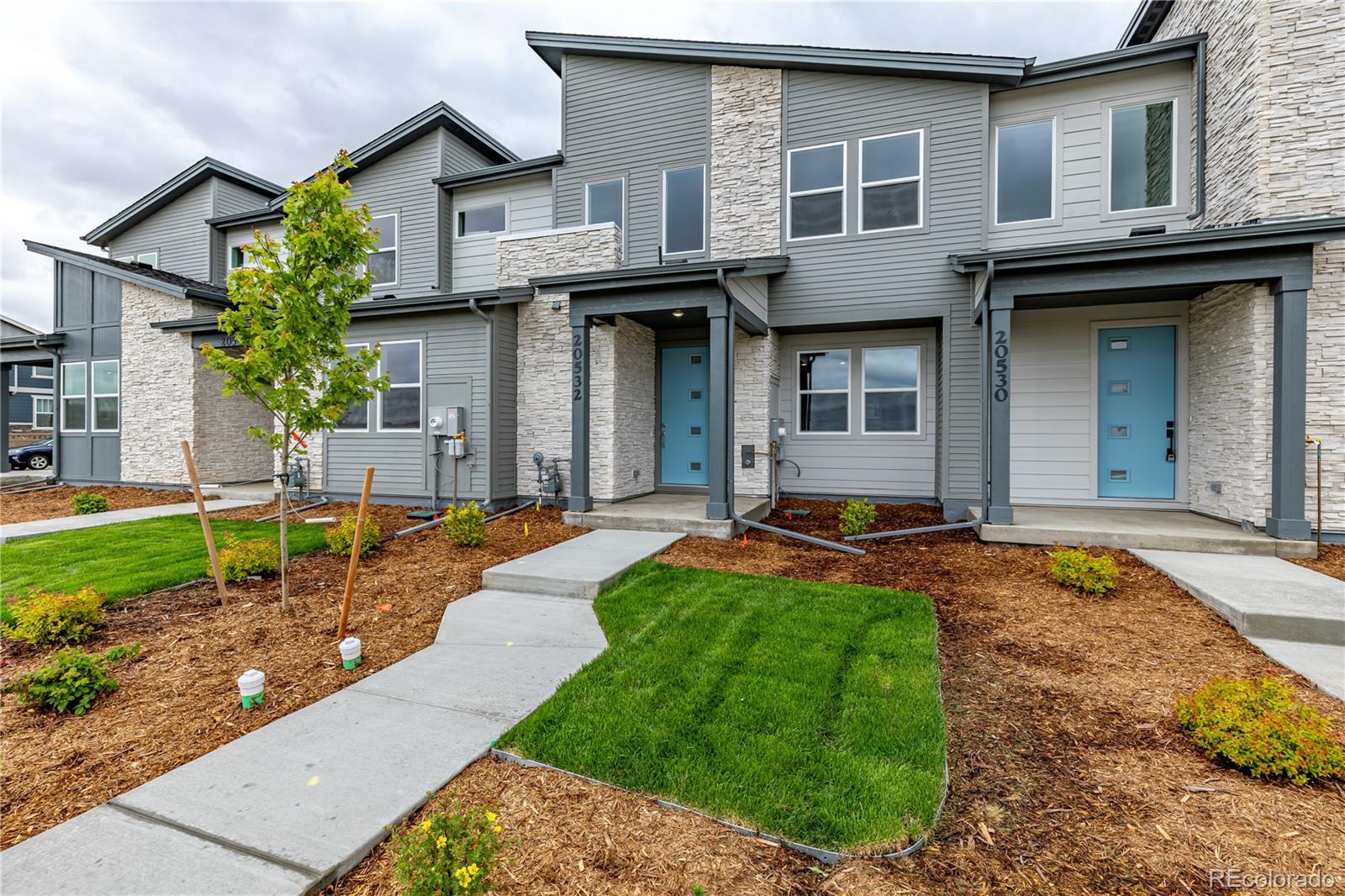 Townhome exterior with gray siding, stone accents, blue doors, and landscaped front walkways.
