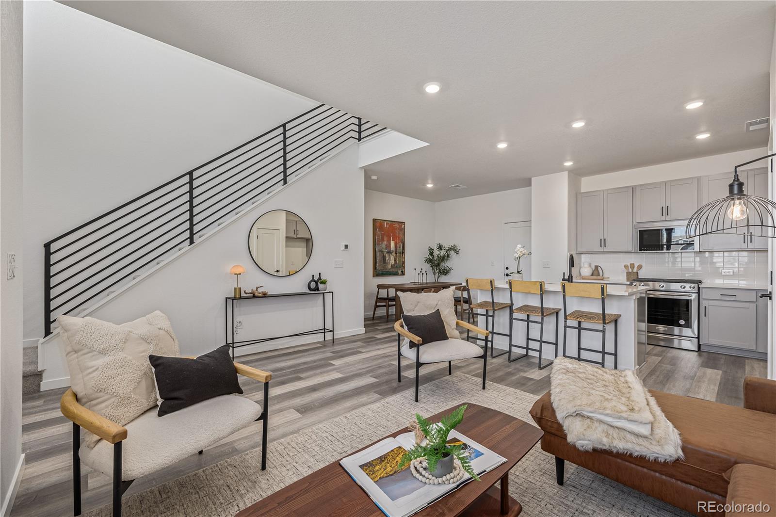 Open-plan living room and kitchen with a black-railed staircase and island seating.