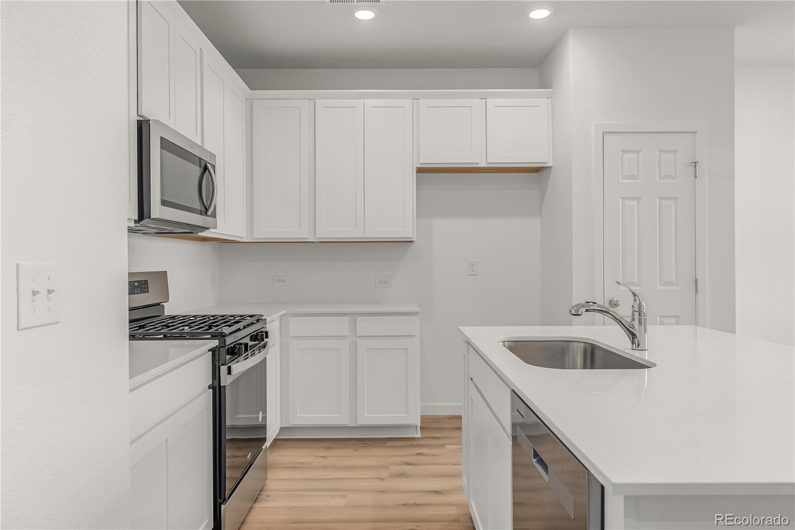 Kitchen with white cabinets, a large island sink, stainless steel appliances, and light wood floors.