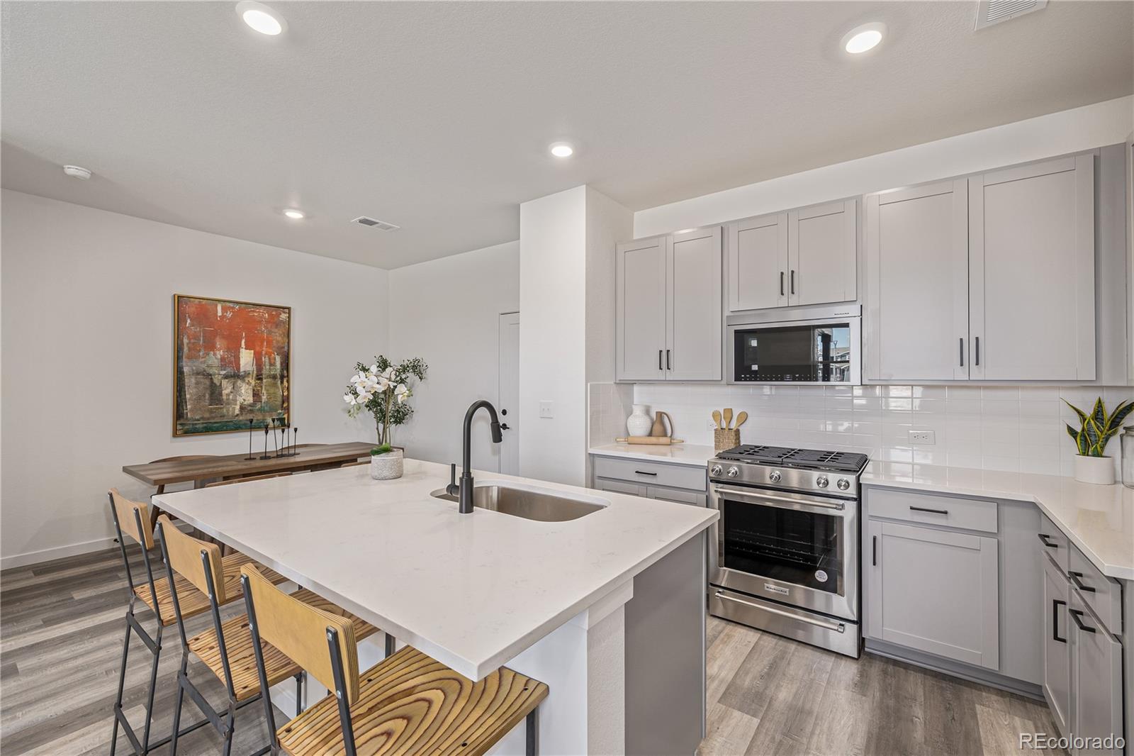 Modern kitchen with white cabinets, stainless steel appliances, and a large island with wood-seat stools.