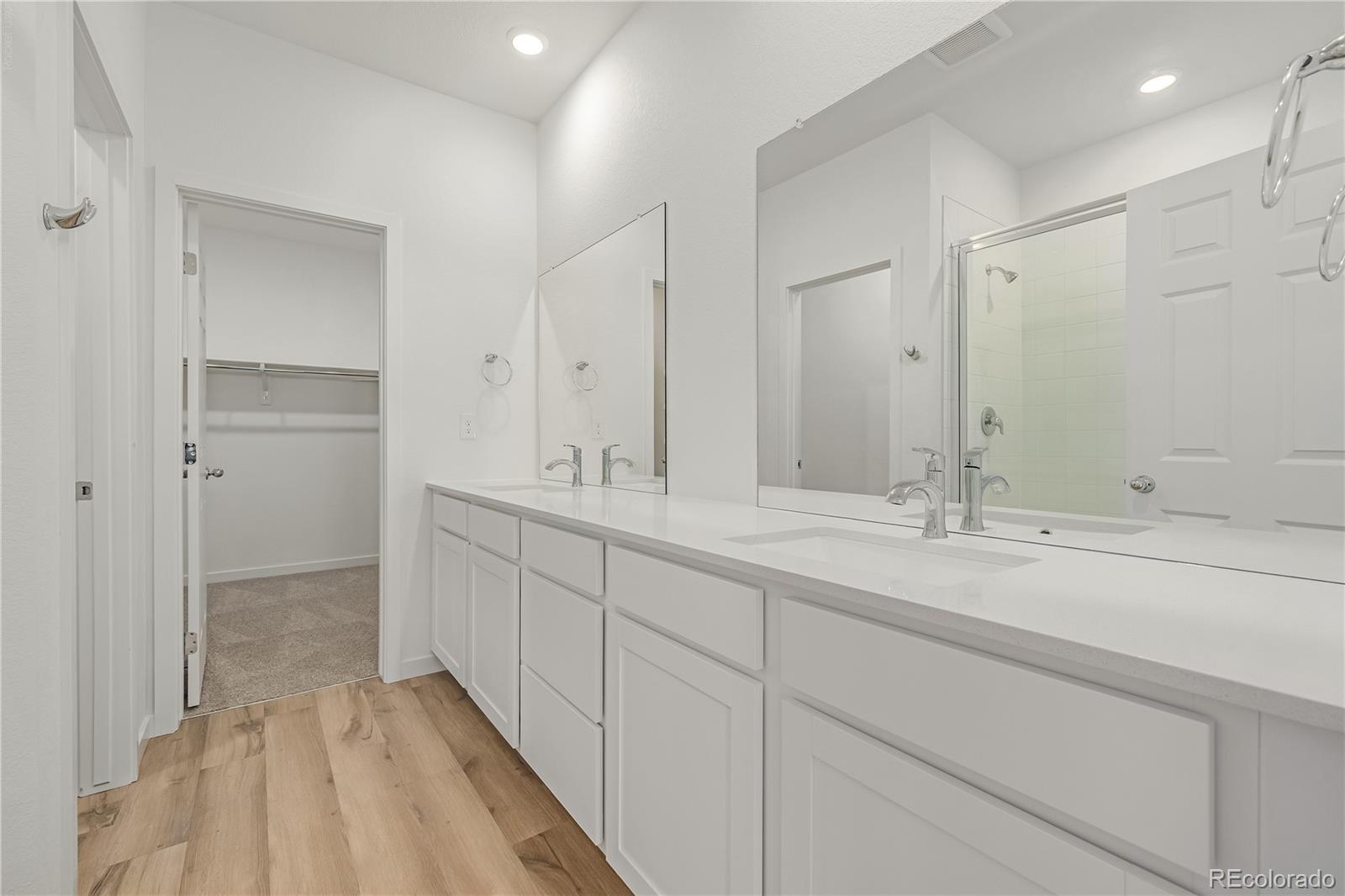 Bathroom with a long double-sink vanity, mirrored wall, and doorway to a walk-in closet.