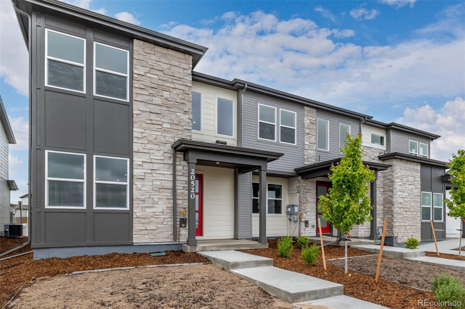 Modern gray-and-stone attached home with tall windows, red doors, and a front walkway.