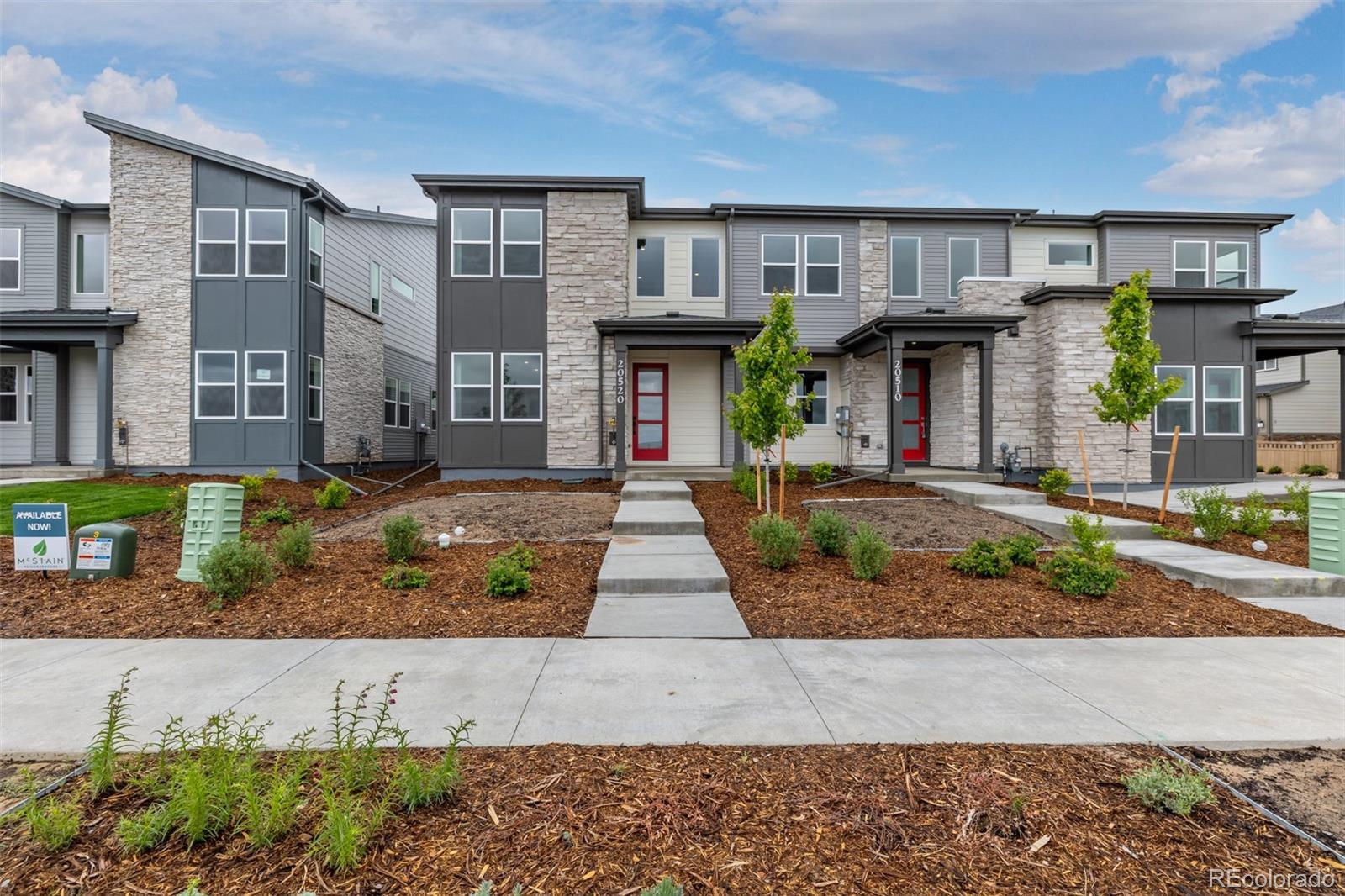 Modern gray townhome with stone accents, a red front door, and a walkway through landscaped mulch beds.