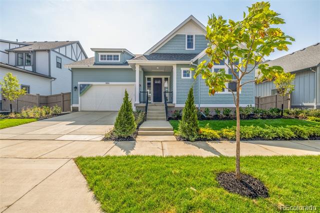 Blue-gray two-story home with a double garage, covered entry, and young tree in the front lawn.