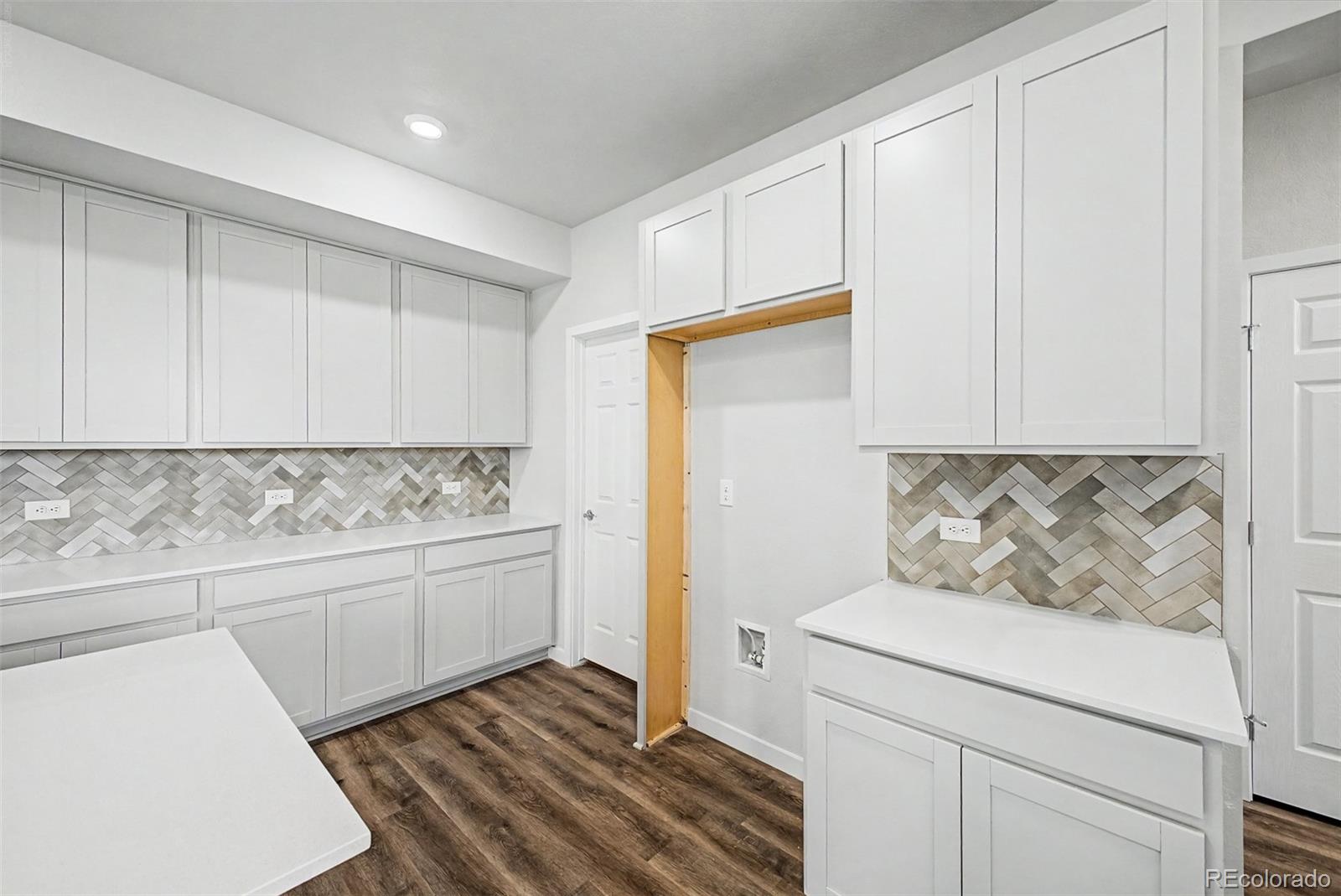 Laundry room with white cabinetry, herringbone tile backsplash, wood-look floors, and appliance hookups.