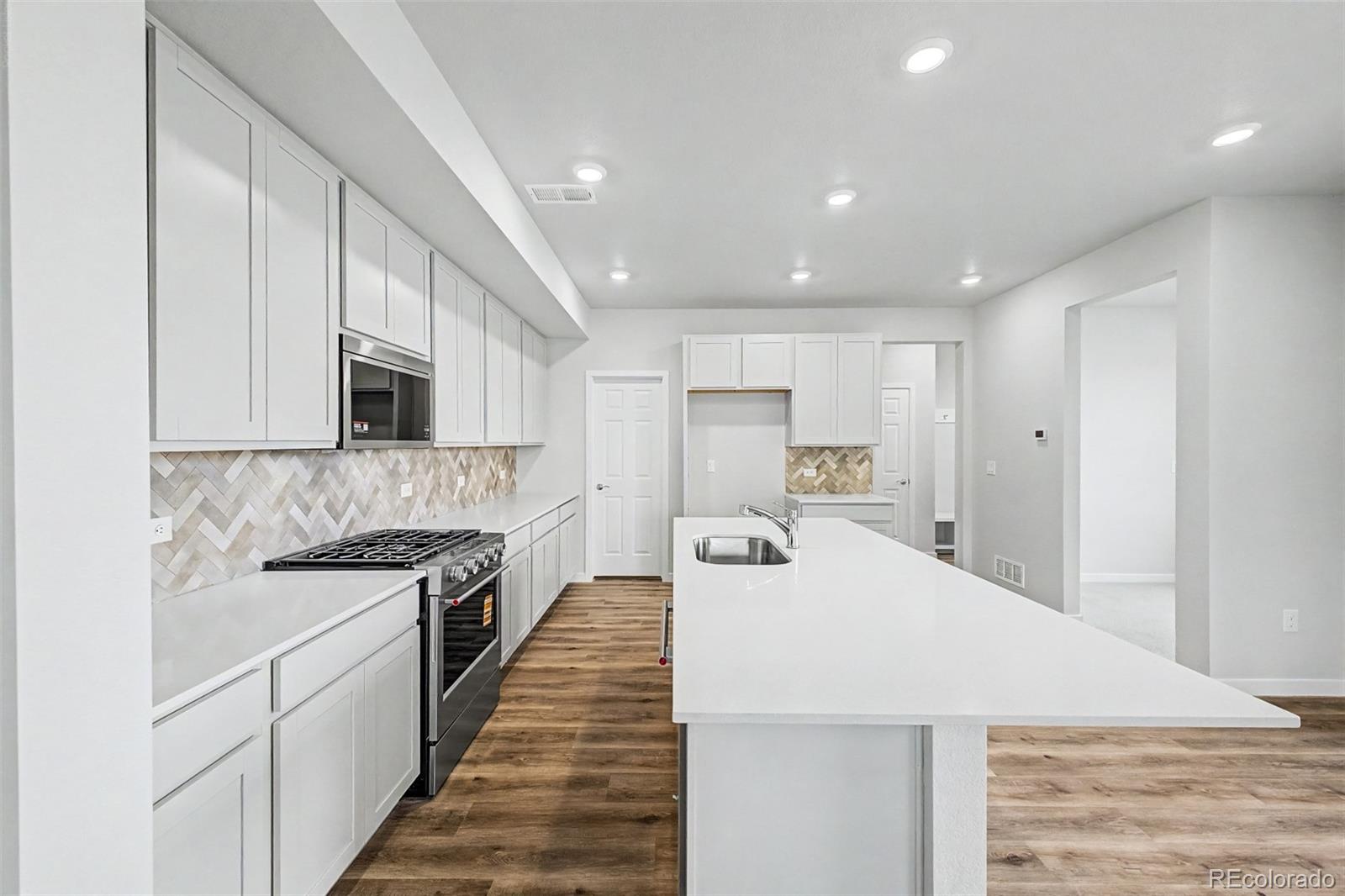 Bright kitchen with white cabinetry, a large sink island, gas range, and herringbone backsplash.