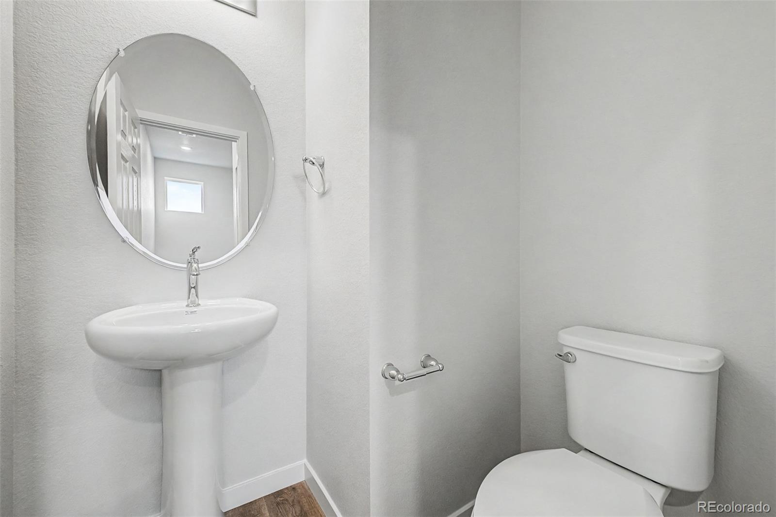 Bathroom with a pedestal sink, round mirror, and white toilet.