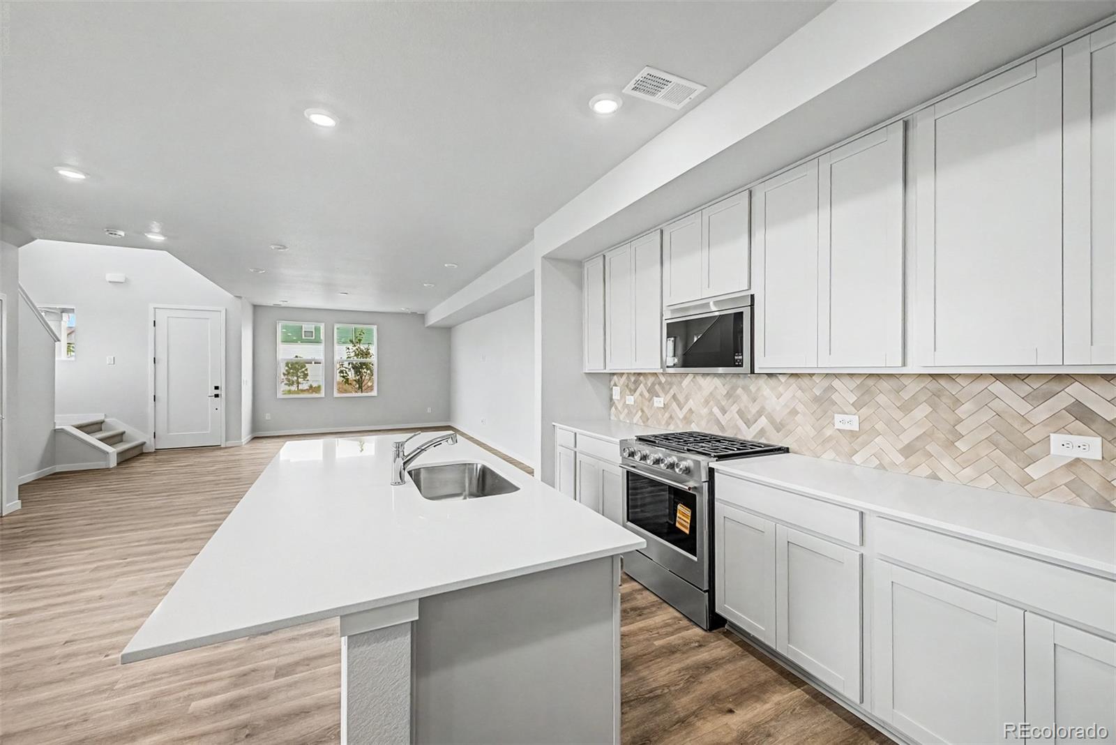 Bright kitchen with white cabinets, a large sink island, and a herringbone tile backsplash.