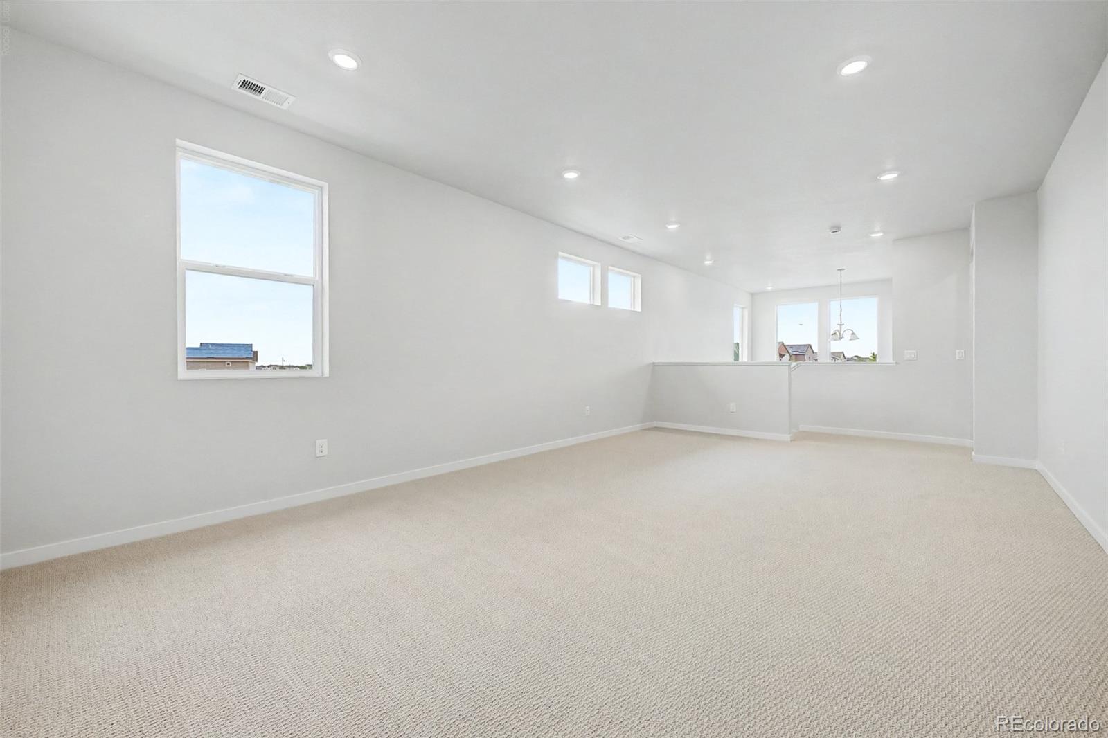 Empty carpeted room with white walls, recessed lights, several windows, and a half-height partition.