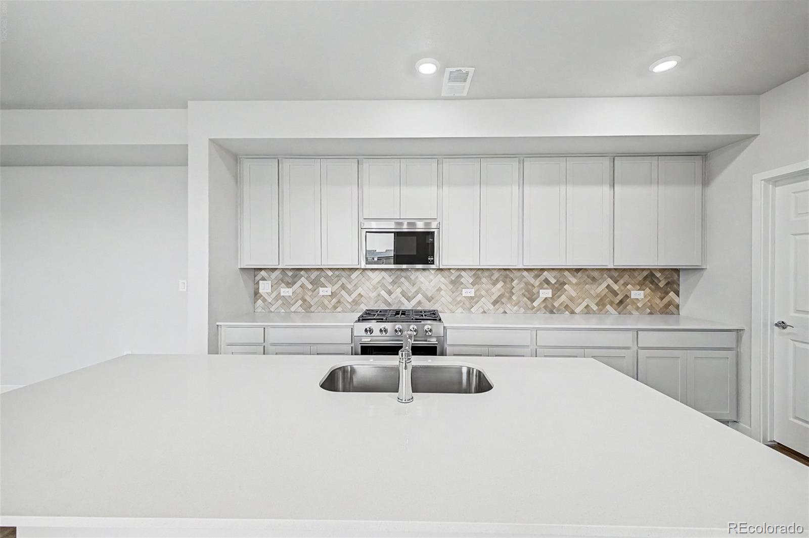 Vacant kitchen with a large white island, patterned backsplash, and stainless steel range.