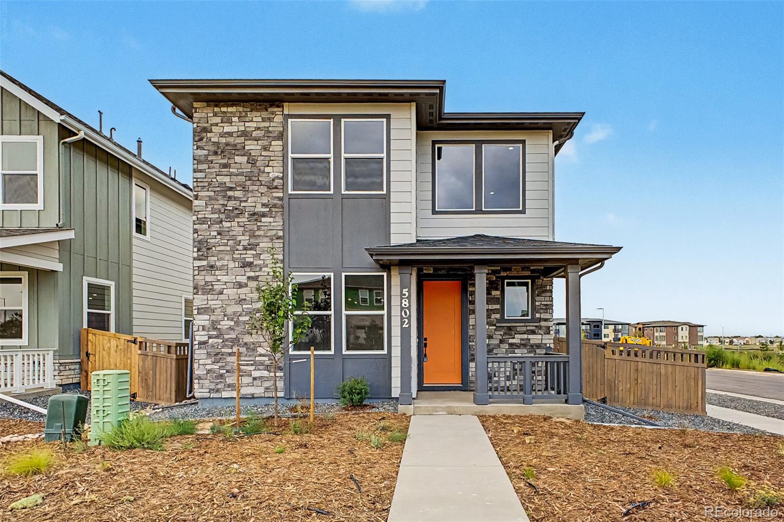 Two-story home with a stone facade, orange front door, covered porch, and concrete walkway.