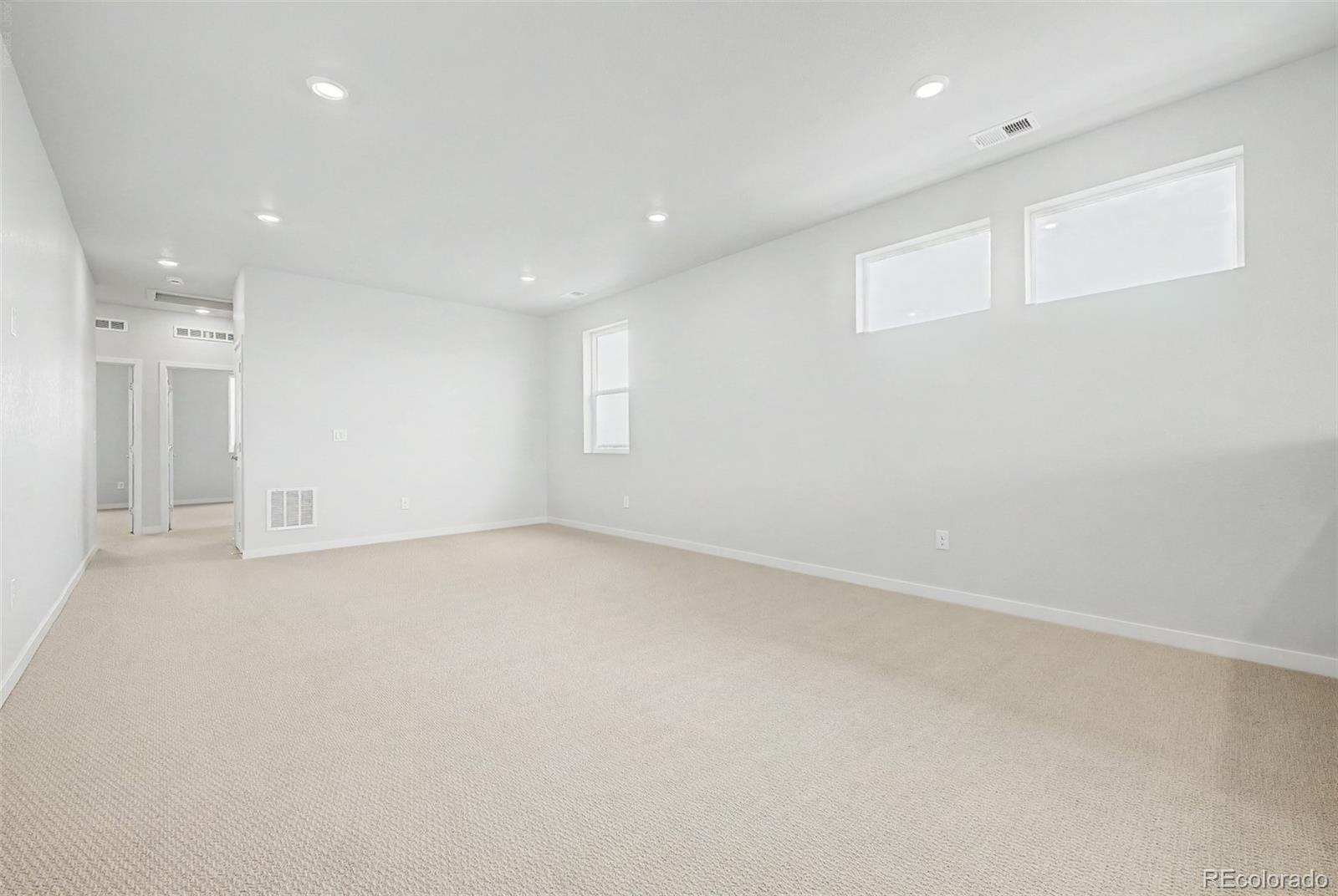 Empty carpeted room with recessed lights, high windows, and doorways to adjoining spaces.