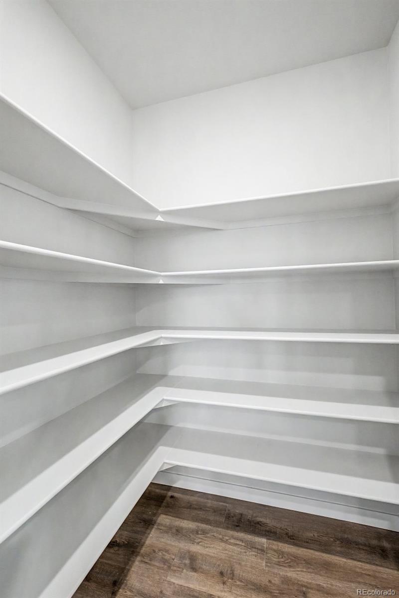 Walk-in pantry with white wraparound shelves and dark wood-look flooring.