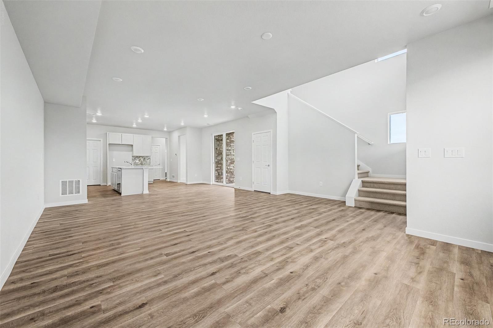 Open-plan living area with wood-look floors, white kitchen island, and carpeted staircase.